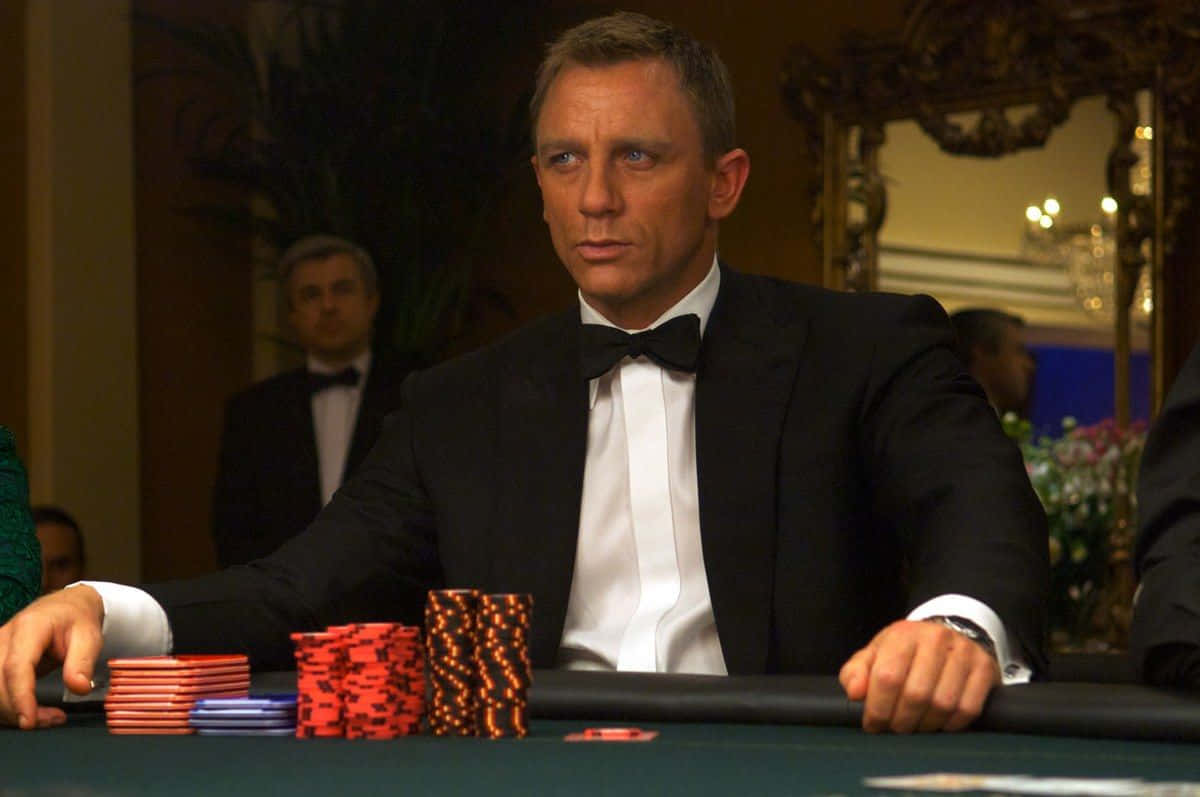 007金手指丹尼爾·克雷格圖 壁紙 — 丹尼爾·基克飾演占士邦，身穿禮服，在賭場撲克桌上專注地看著一堆紅色和藍色籌碼。