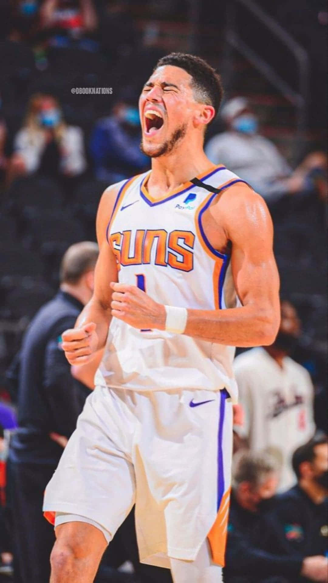 1. NBA球星德文·布克持iPhone投籃 壁紙 — 一位鳳凰城太陽隊籃球運動員在比賽中握緊拳頭，身後人群模糊，勝利地吶喊。