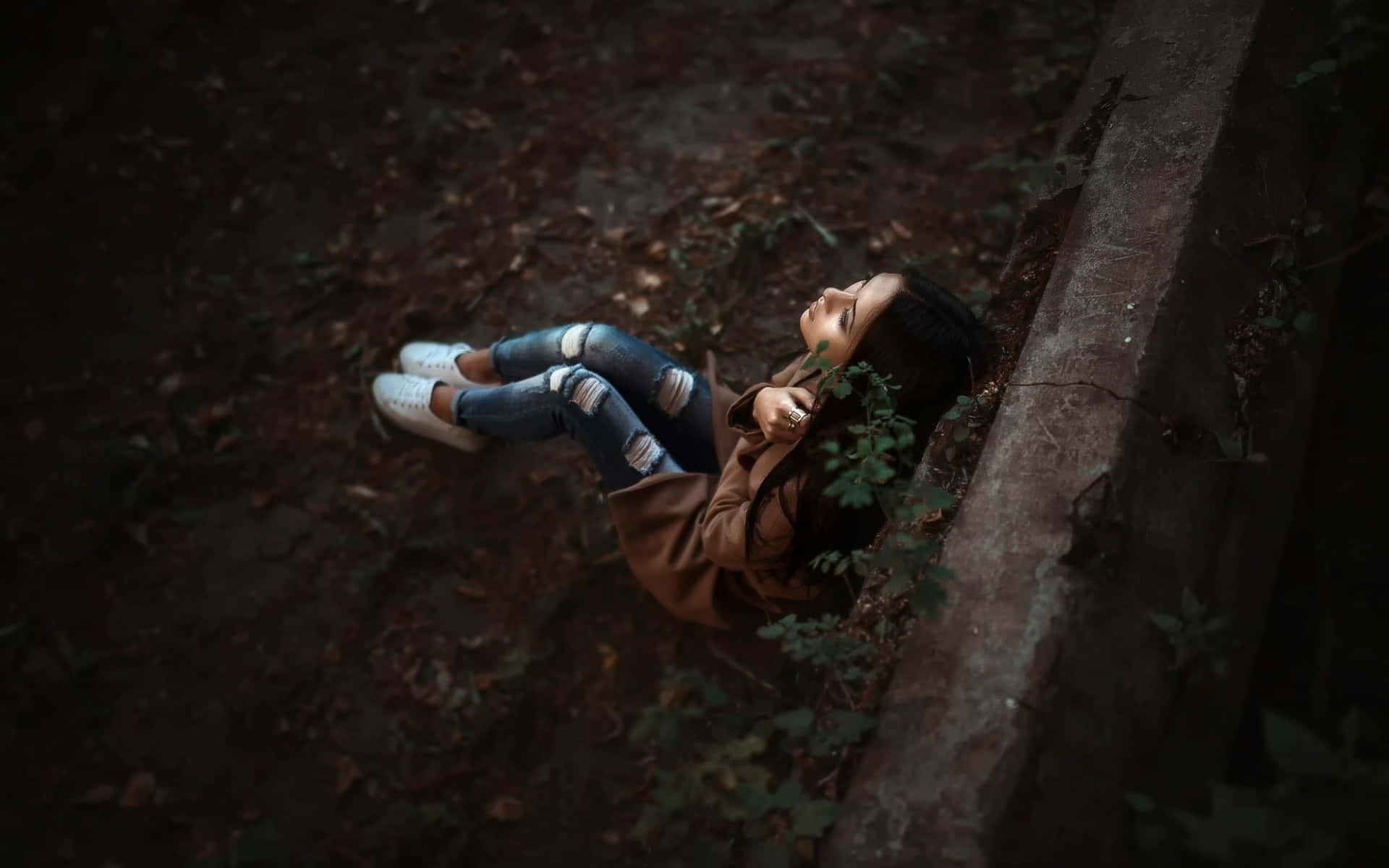 年輕女性躺在森林地上，旁邊有一塊長滿苔蘚的石頭，冷靜地向上看。