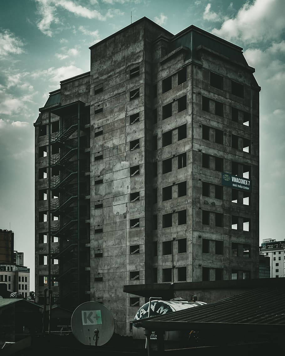 1080p高清廢棄大樓 壁紙 — 一座高聳的廢棄混凝土建築，窗戶破損，設有外部樓梯，矗立在多雲的天空下。