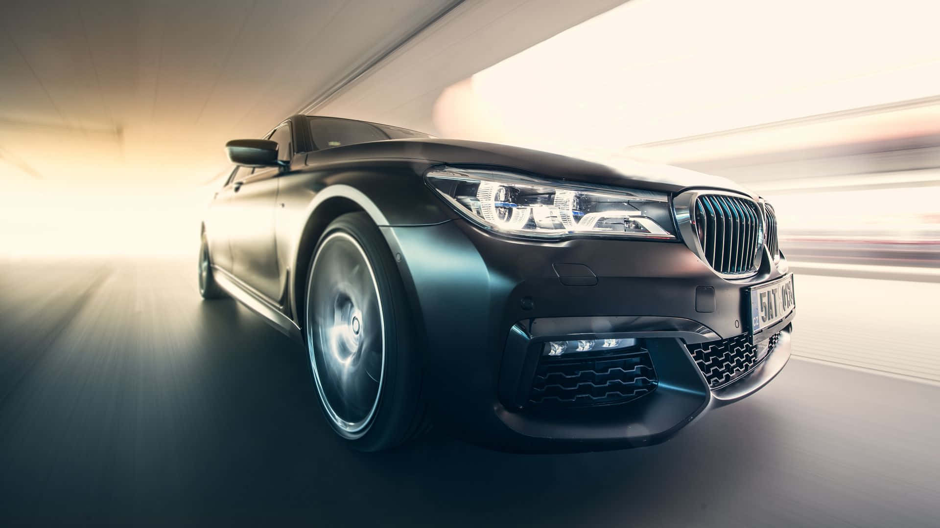 1080p M系列背景：磨砂黑BMW 7系 壁紙 — 一輛時尚的黑色寶馬房車在隧道中疾馳，動態模糊掠過其發光的車頭燈。