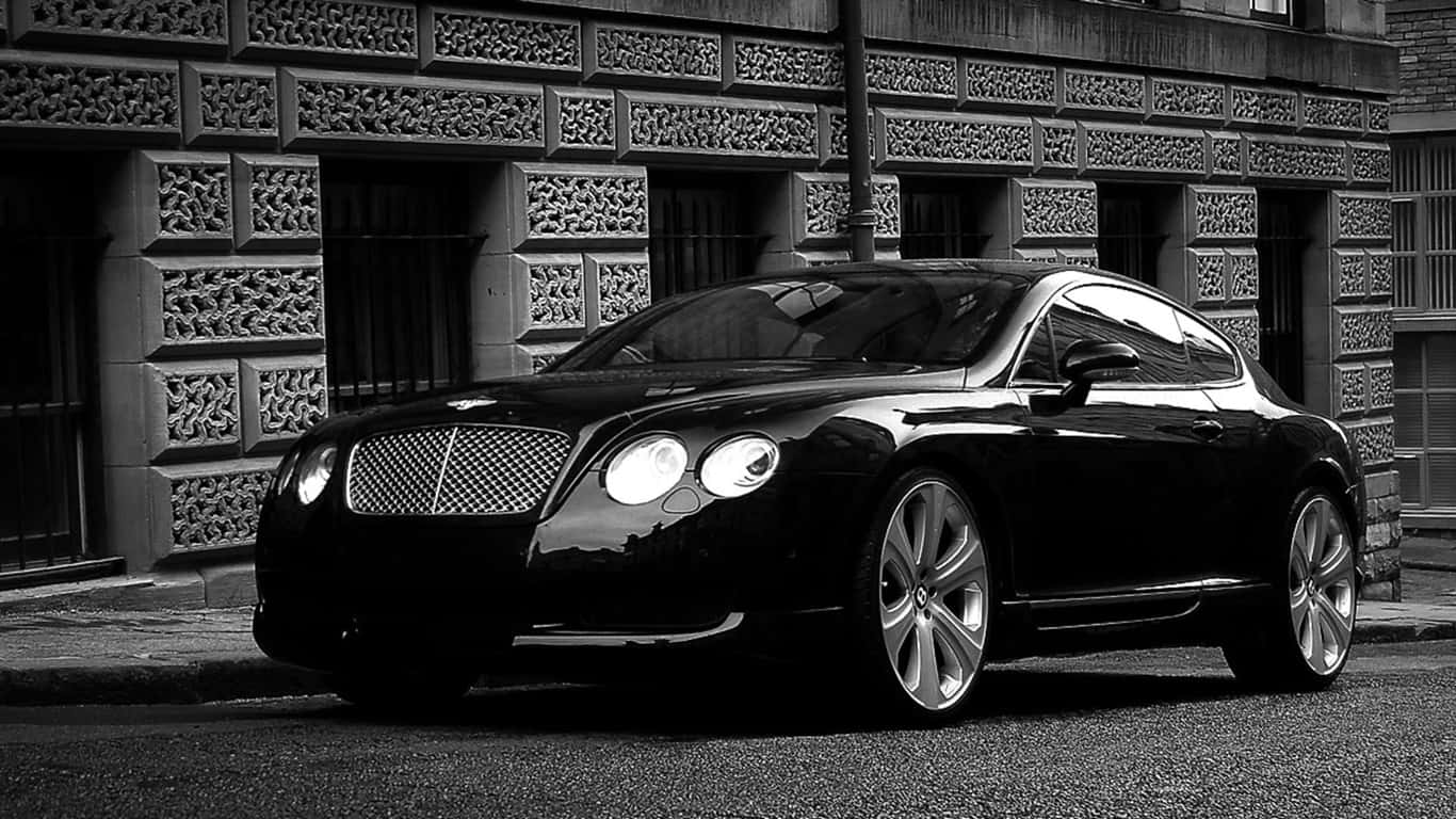 1366x768 黑色2008款賓利轎車背景 壁紙 — 一輛時尚的黑色賓利轎跑車在單色燈光下閃耀，襯托著華麗的石砌建築外牆。