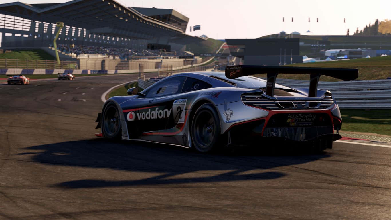 1366x768 Project Cars 2 賽車駕駛截圖 壁紙 — 一輛帶有Vodafone塗裝的銀色賽車，在陽光普照的賽道上飛馳，背景有看台和其他賽車。