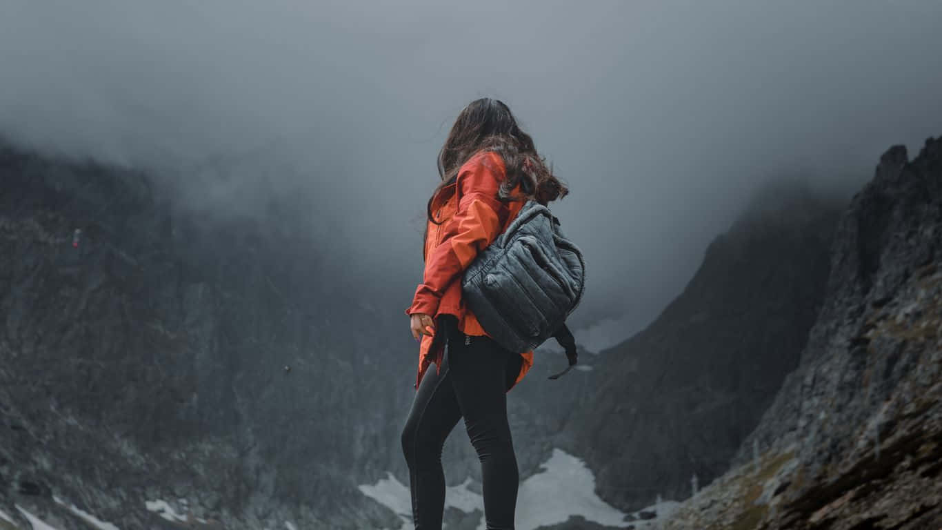 身穿橙色外套的人在霧氣瀰漫的山上遠足，有霧和雪斑。