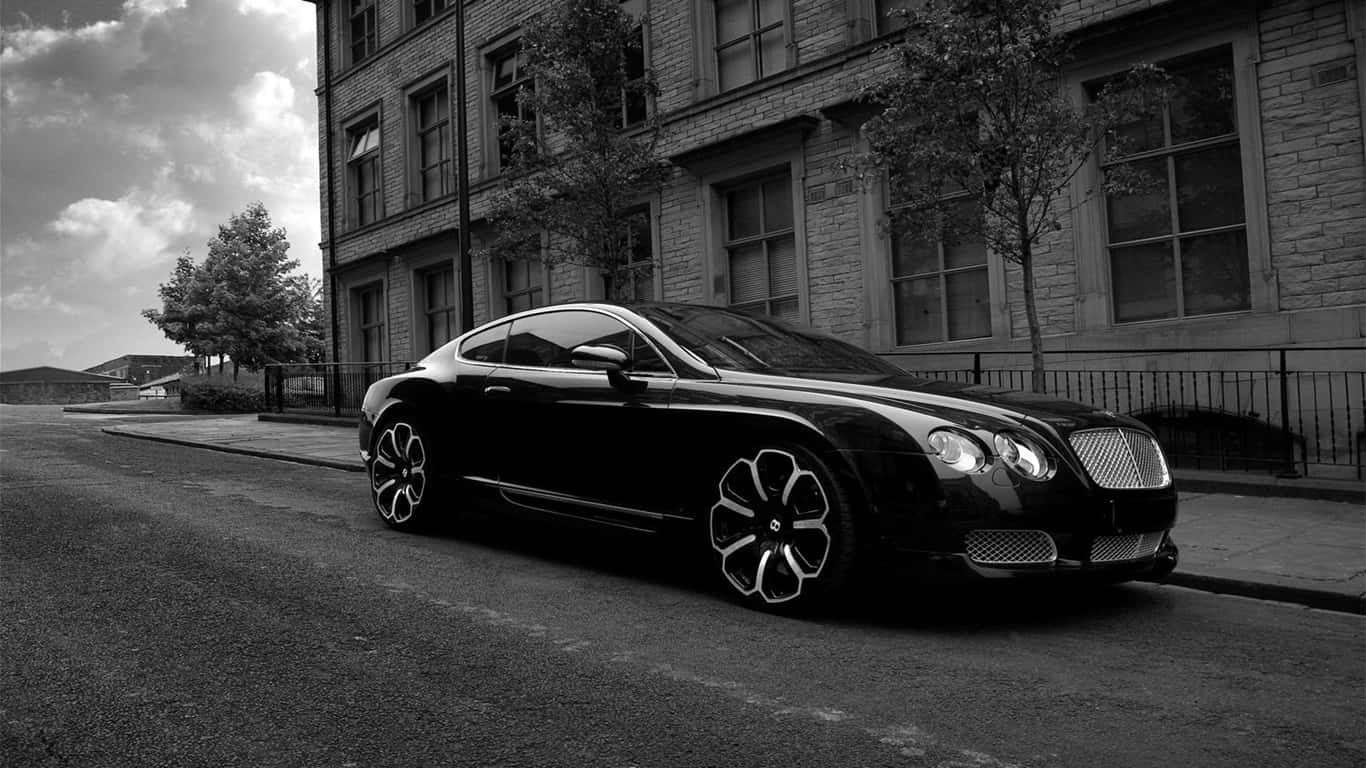 1366x768 宾利背景 — 黑色 Bentley Continental GT 街頭風 壁紙 — 一架時尚的黑色賓利 Continental GT 停泊在城市的街道上，旁邊是一棟磚造建築，天空多雲。