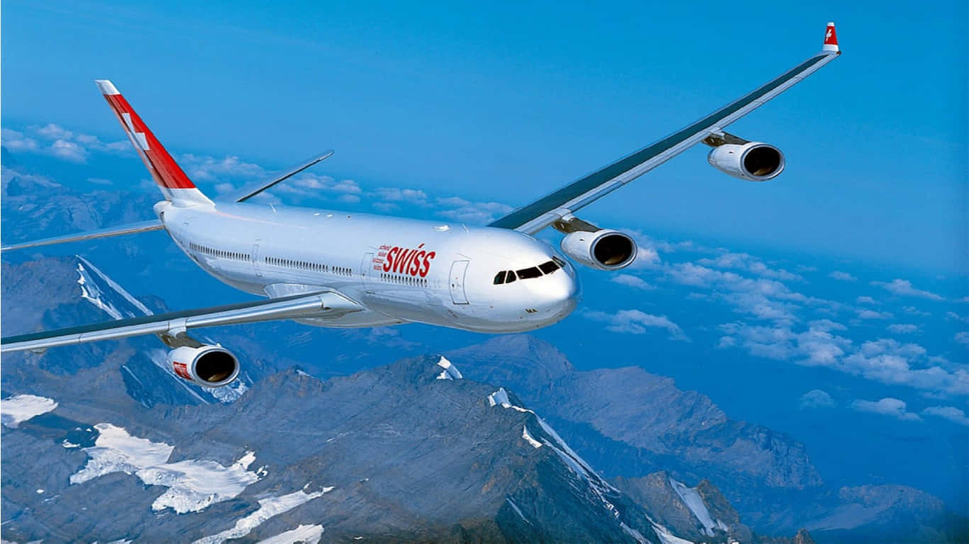 1366x768 巨型客機背景 瑞士國際航空 壁紙 — 一架瑞士空中巴士A340在晴朗藍天與零星白雲下翱翔於積雪的山峰之上。