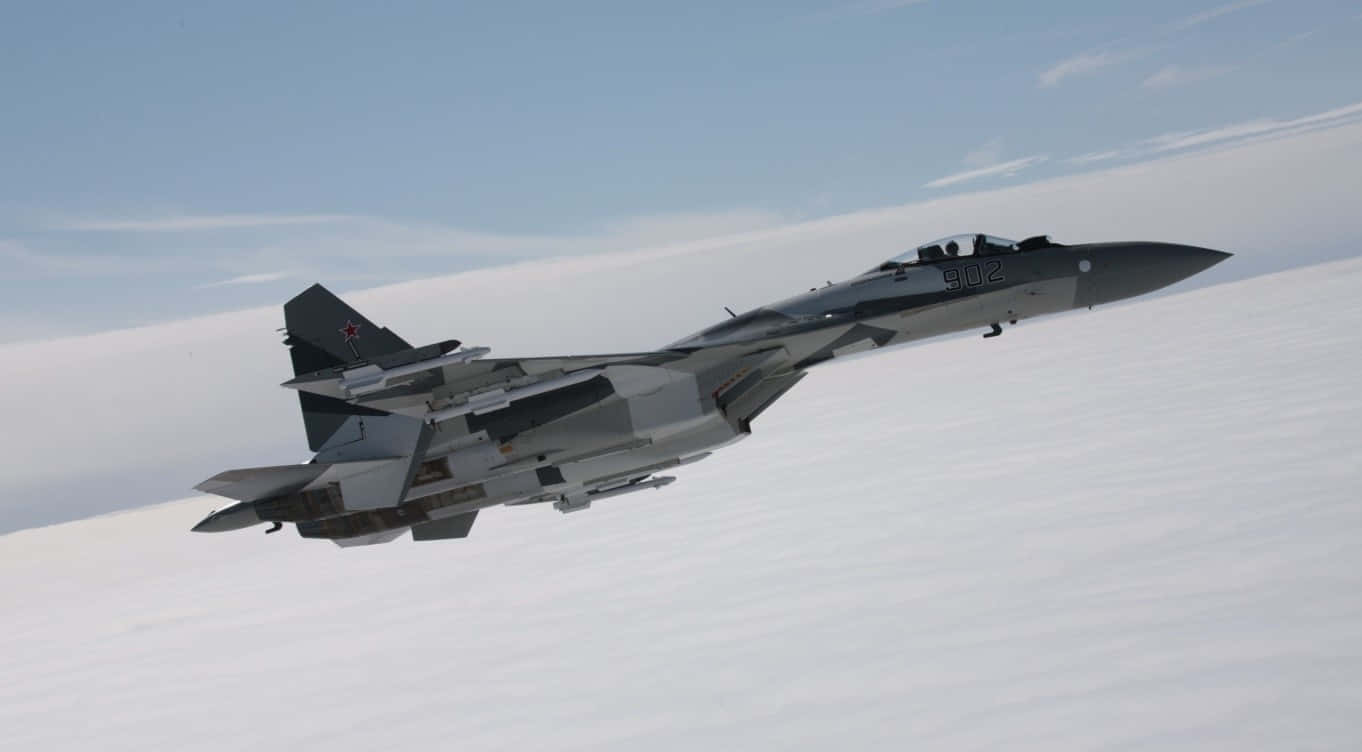 1366x768 巨型客機背景：蘇霍伊 Su-35 壁紙 — 一架灰色戰鬥機在淡藍色天空下翱翔於白色雲層之上。