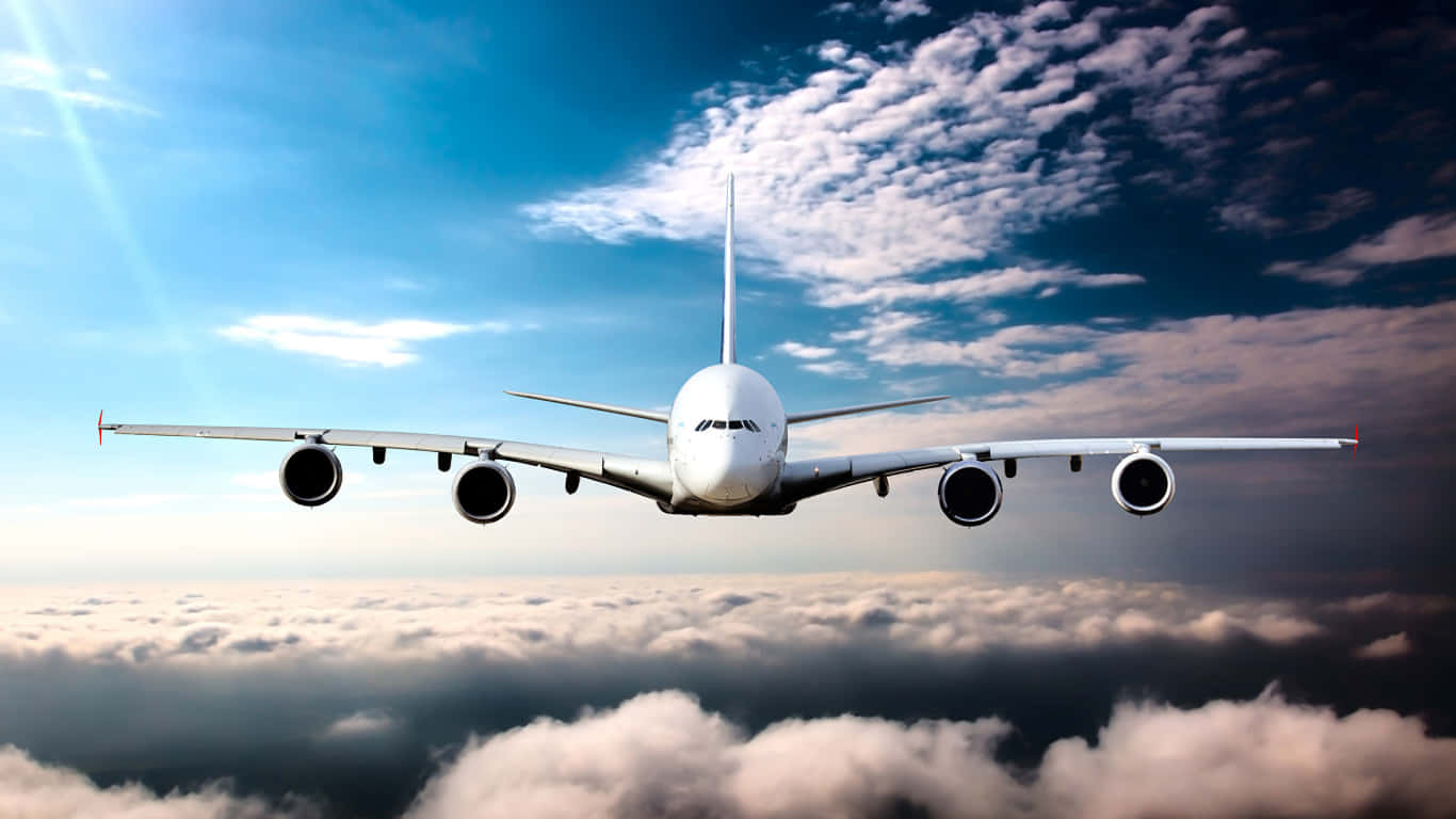 1366x768 巨型客機背景 飛機正面 壁紙 — 一架白色珍寶客機在陽光穿透的湛藍天空下，翱翔於蓬鬆雲層之上。