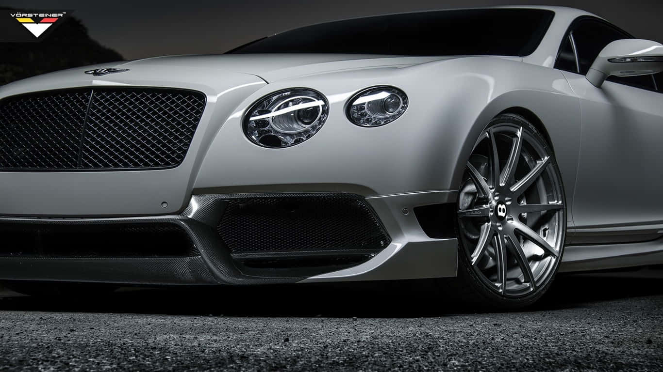 1366x768 白色賓利 Continental GT3 背景 壁紙 — 一輛時尚的銀色賓利跑車，配備定制輪轂和碳纖維飾件，在戲劇性燈光下停在瀝青路面上。
