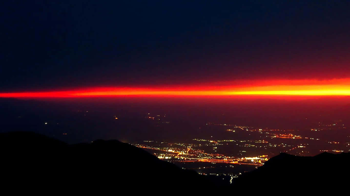 夜間在發光的紅色地平線下的城市燈光，前景有黑暗的山丘。