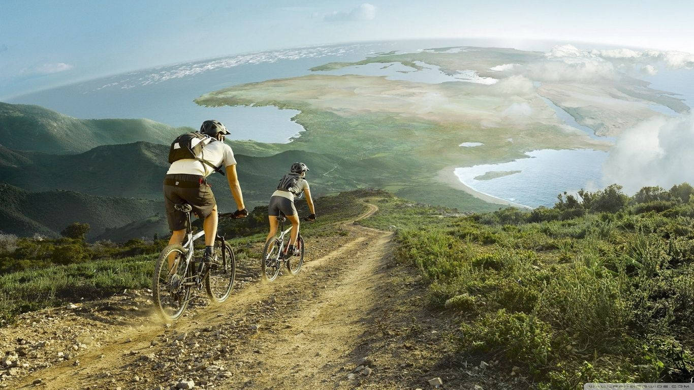 兩名騎單車人士在泥路上騎行，下方是風景優美的山谷和水域。