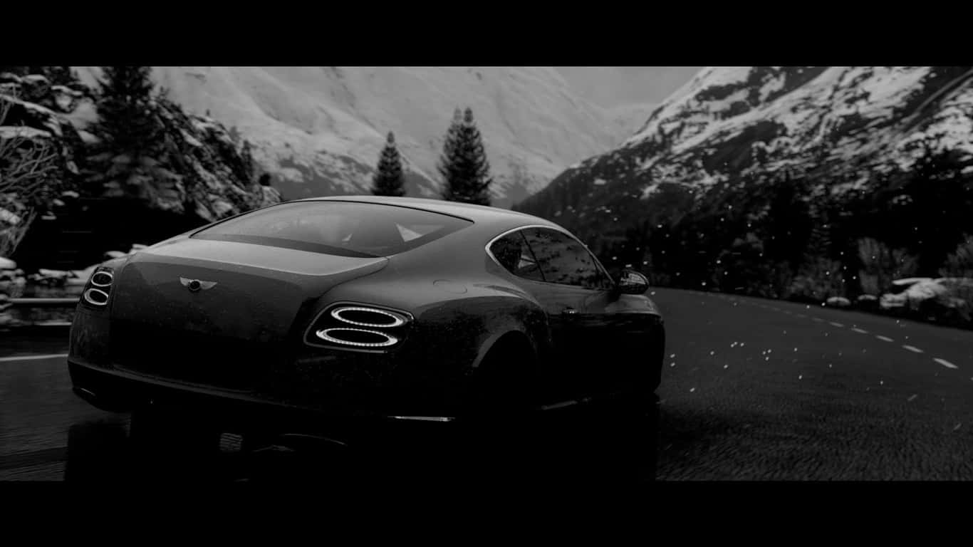1366x768 黑色 2017 賓利 Continental GT 山景背景 壁紙 — 一輛時尚的黑色賓利雙門跑車在白雪覆蓋的山路上行駛，沿途有松樹和積雪的山峰，呈現單色調。