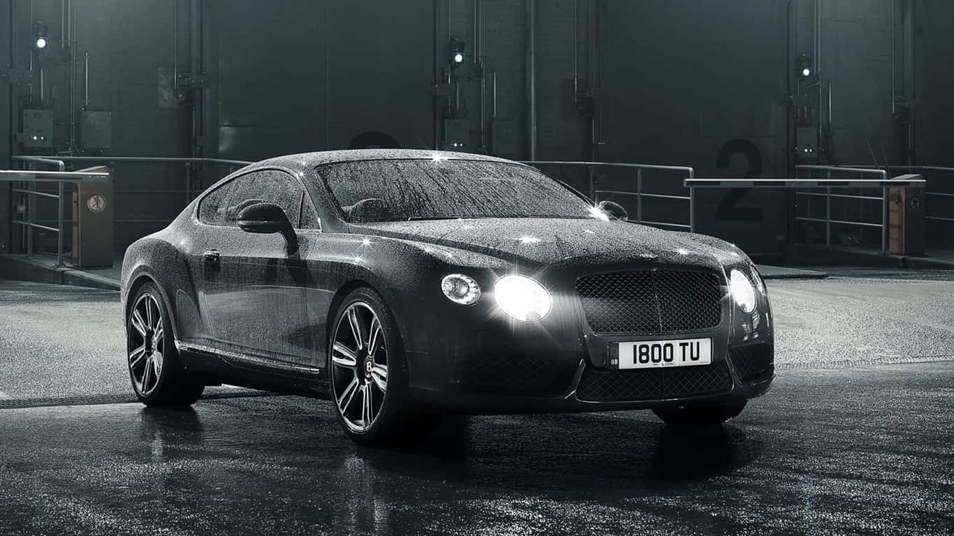 1366x768 黑色2012款賓利轎車背景 壁紙 — 一輛時尚的黑色賓利 Continental GT 在潮濕的工業車庫地板上，在明亮的車頭燈下閃閃發光。