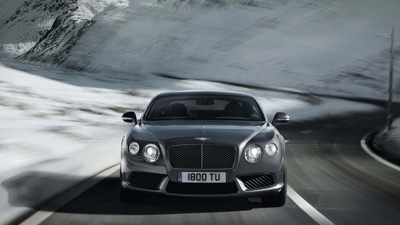 1366x768 黑色2018款賓利轎車背景 壁紙 — 一輛時尚的銀色賓利 Continental GT 在蜿蜒的積雪山路上疾馳，帶有模糊的動感。