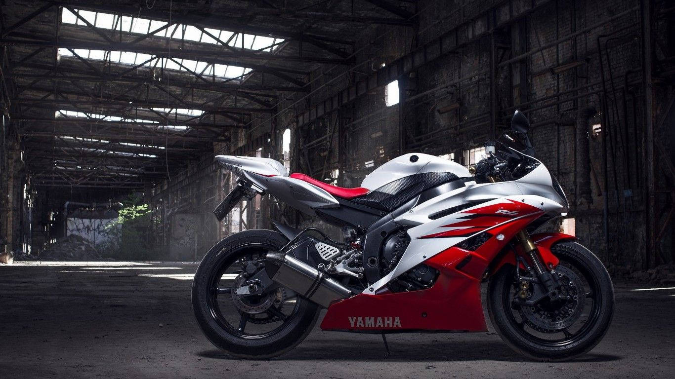 13688 x 768 高清運動 壁紙 — 一架流線型的紅白Yamaha電單車，停泊在陽光普照的廢棄工業倉庫中。