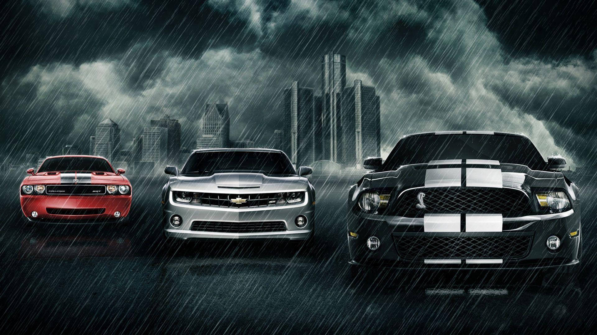 13688X768 高畫質運動背景主題 壁紙 — 三輛強力肌肉車在暴風雨的城市環境中向前行駛，雨水劃過黑暗的天空和背後的城市天際線。