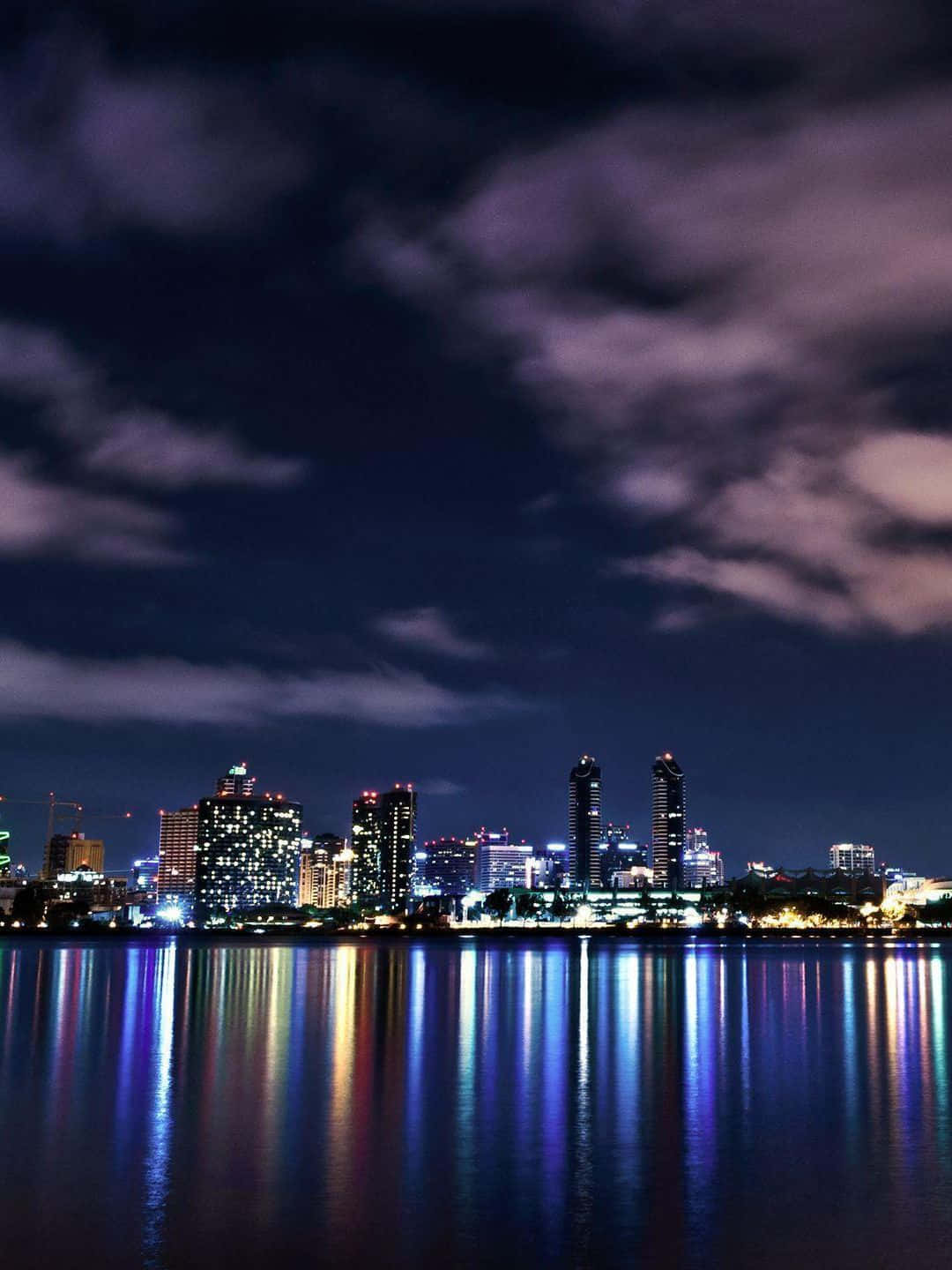 1440p 聖弗朗西斯科夜景天際線 壁紙 — 在戲劇性的多雲天空下，寧靜的水面倒映著充滿活力的城市夜景。
