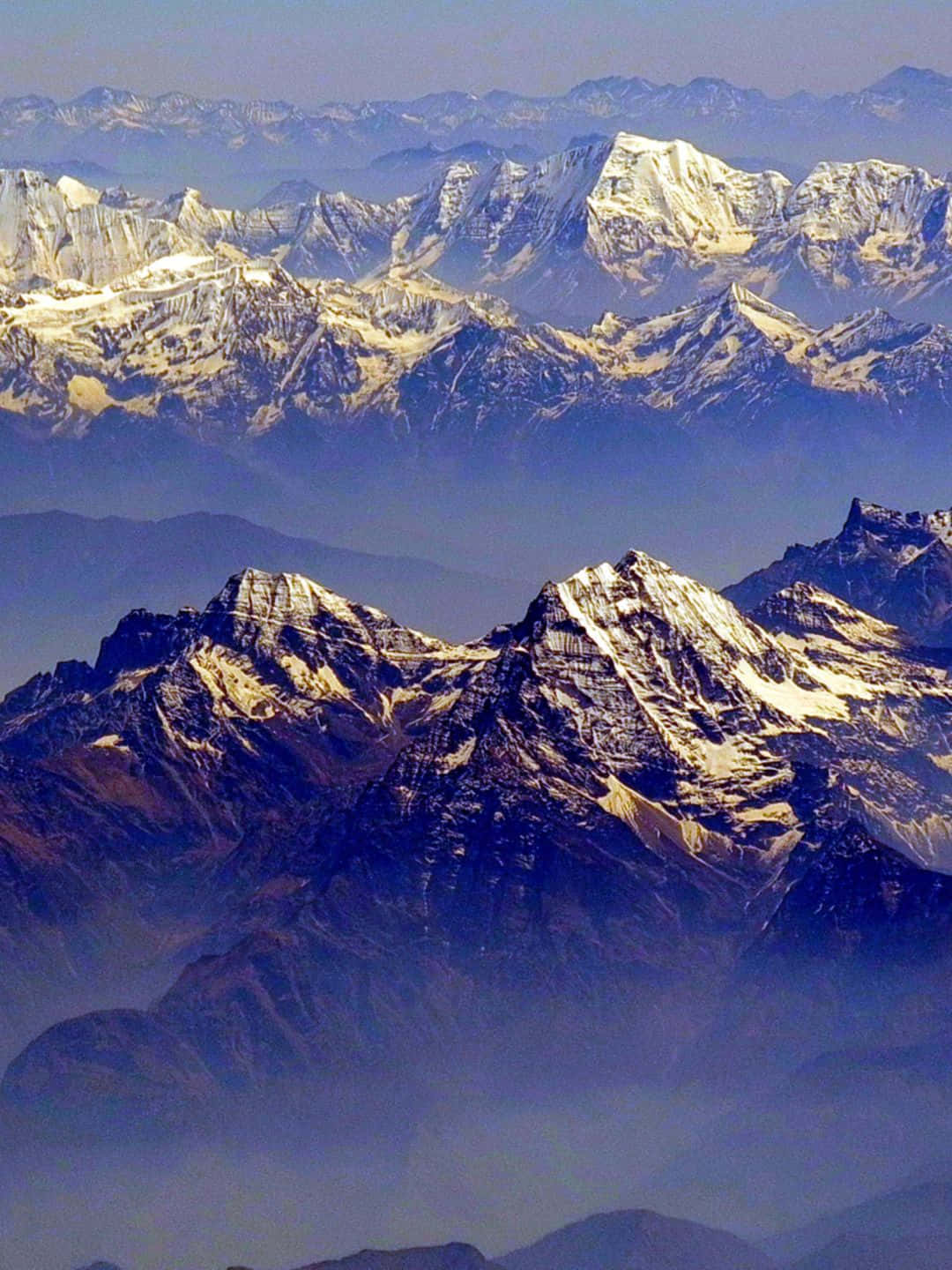 1440p 自然背景：雲霧繚繞的喜馬拉雅山脈 壁紙 — 在清澈藍天下，層層疊疊的積雪山脈逐漸融入大氣薄霧中的鳥瞰圖。