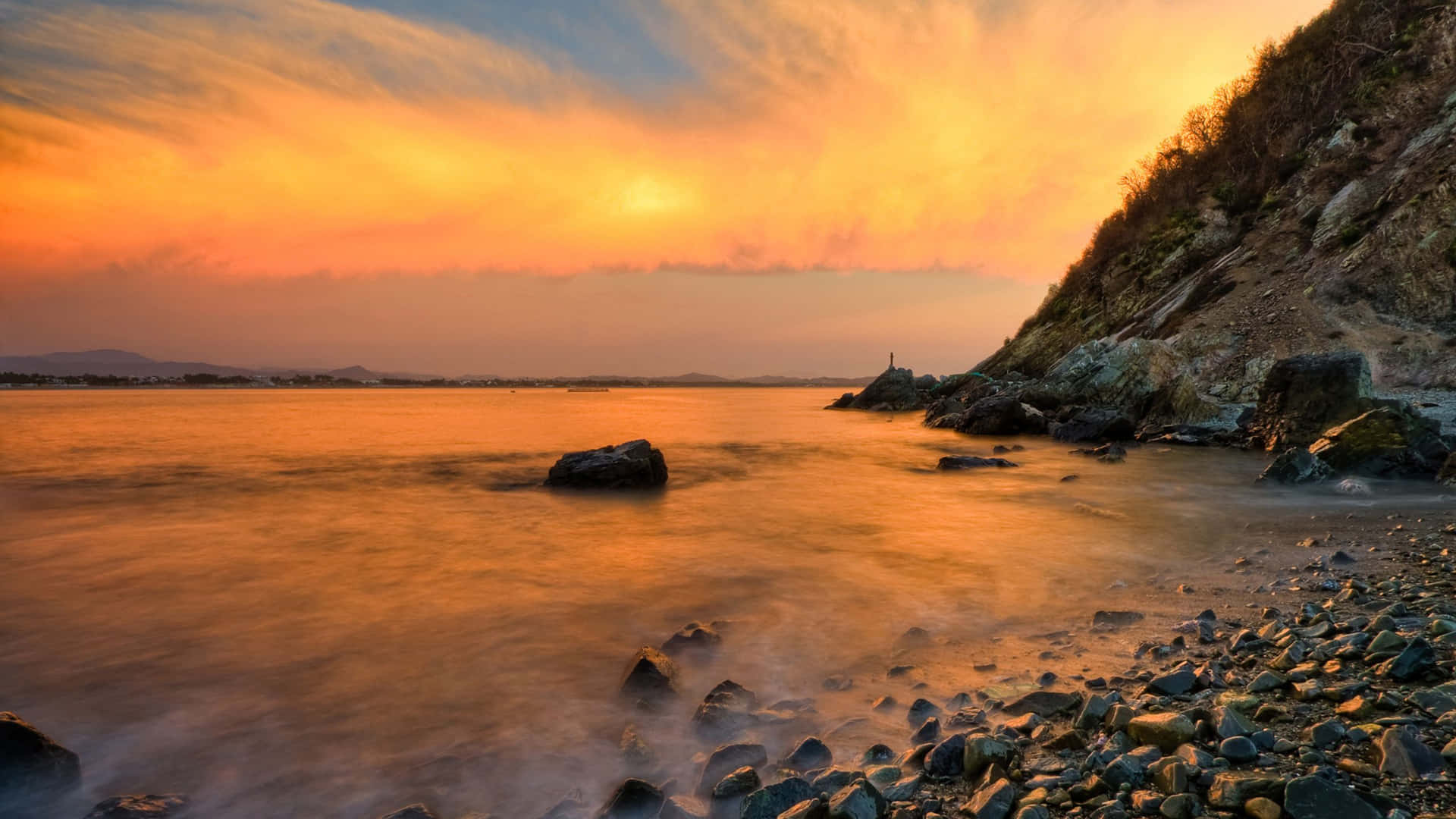 平靜水面上的金色夕陽，岩石海岸與遠方山丘