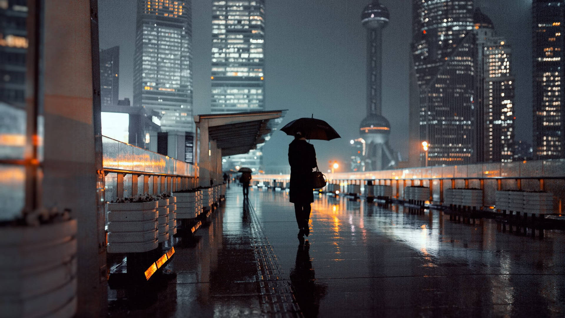夜晚雨中城市人行道上撐傘行走的人，帶有倒影。