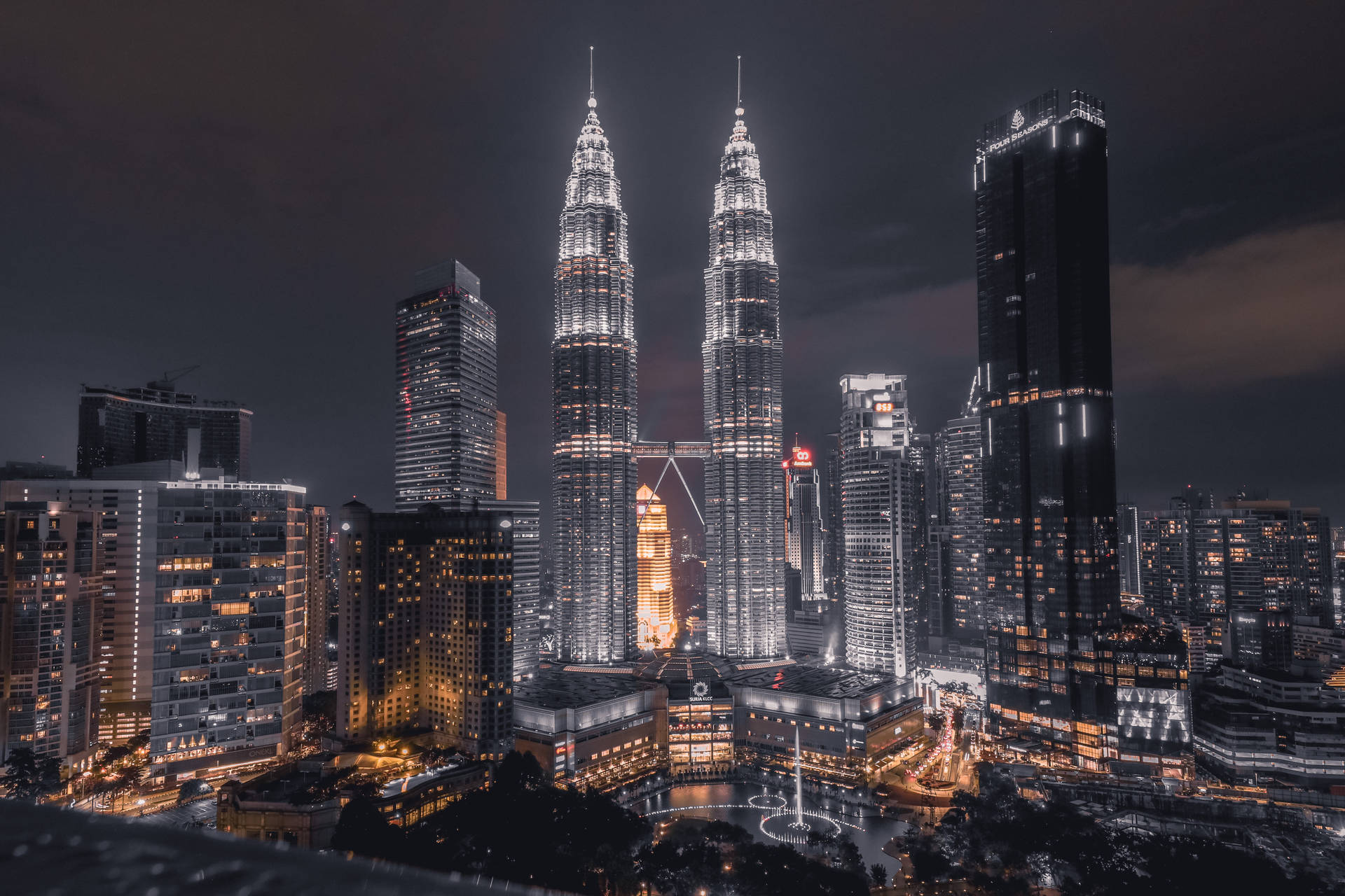 Nighttime cityscape featuring iconic twin towers and surrounding skyscrapers lit up with warm lights.