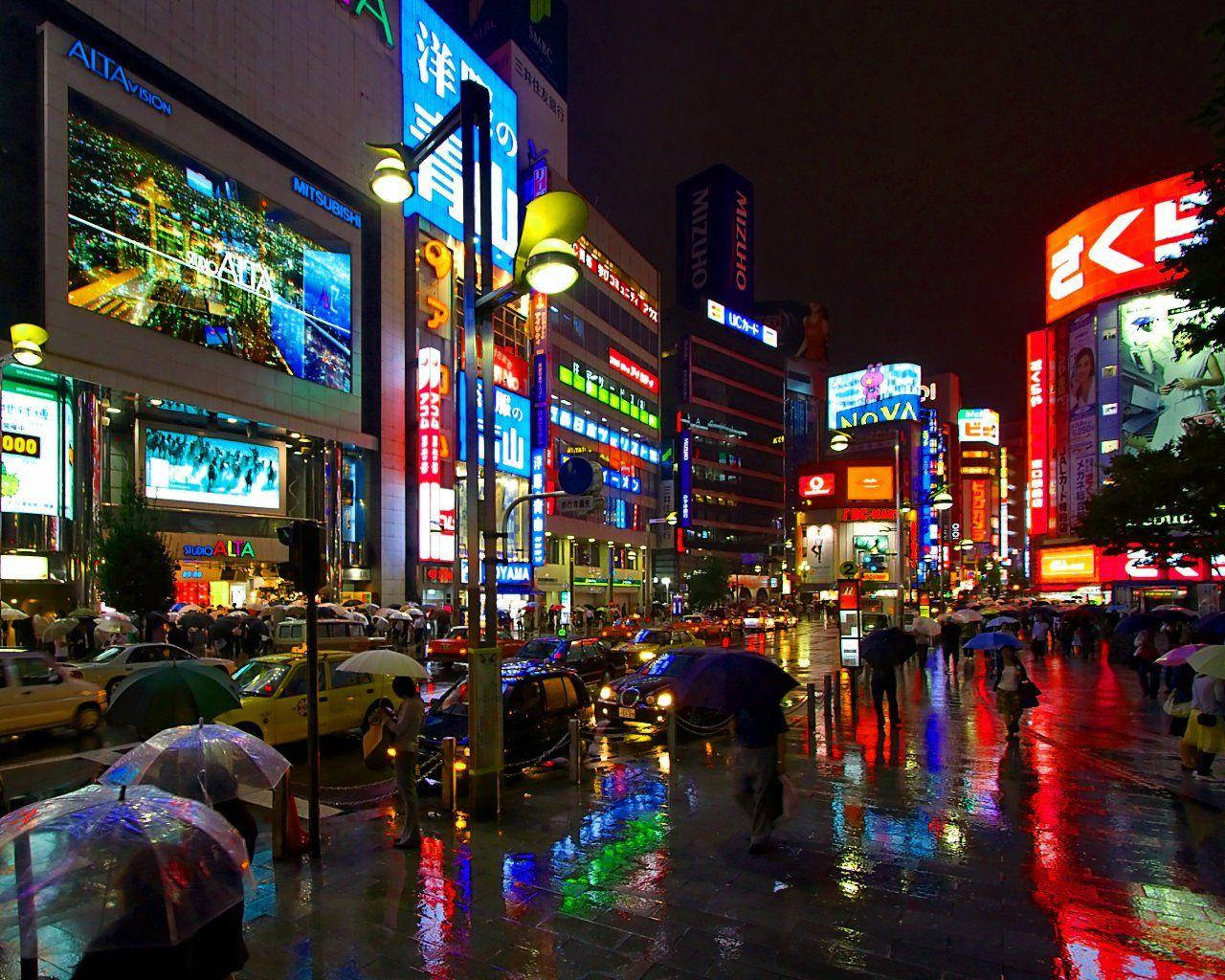繁忙的東京夜晚街道，霓虹燈在濕漉漉的人行道上反射，人們撐著傘。