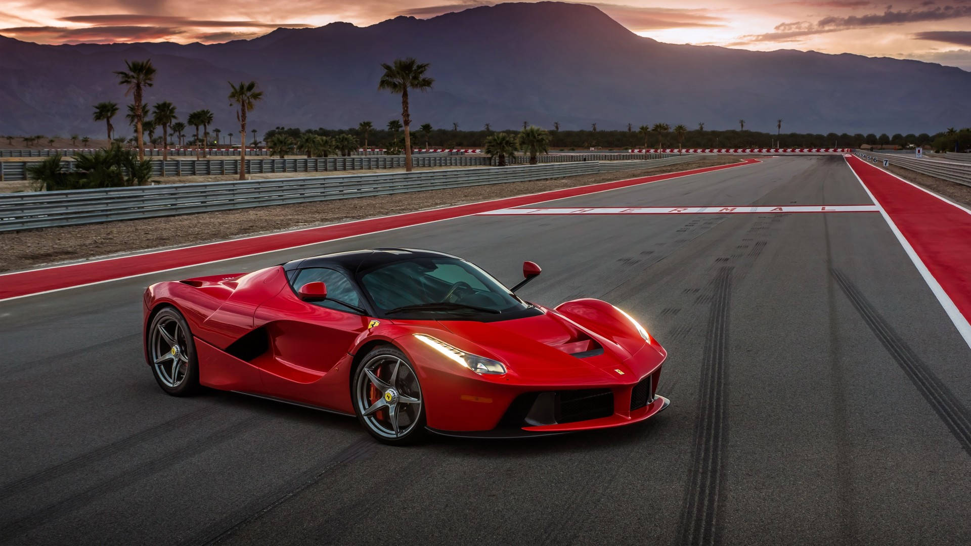 2014 年 1920x1080 Ferrari LaFerrari 紅色款 壁紙 — 一輛鮮紅色的法拉利 LaFerrari 在日落時分沿著賽道飛馳，背景有棕櫚樹和山脈。