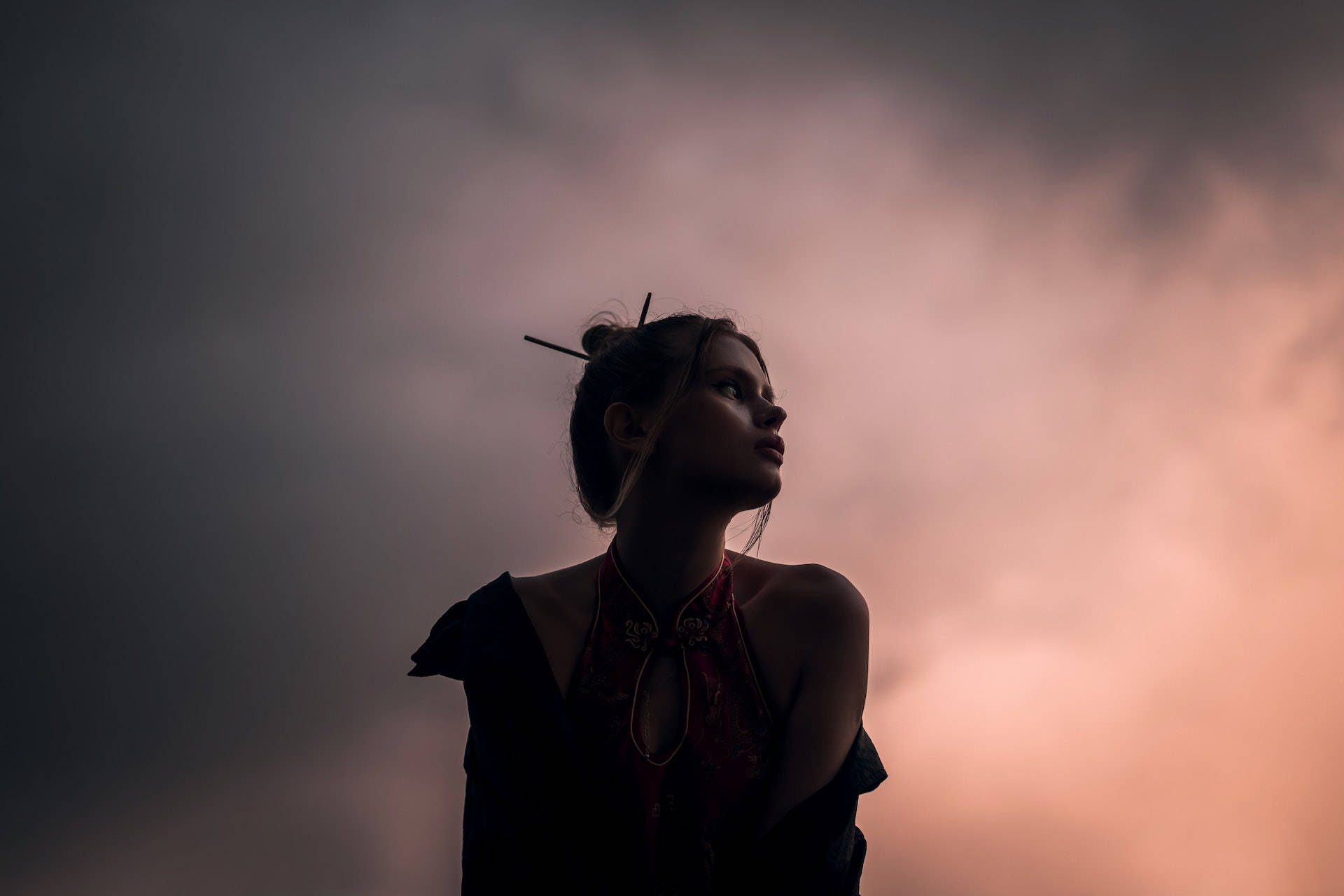 剪影中的女人看著帶有粉紅色和灰色雲彩的黃昏天空。