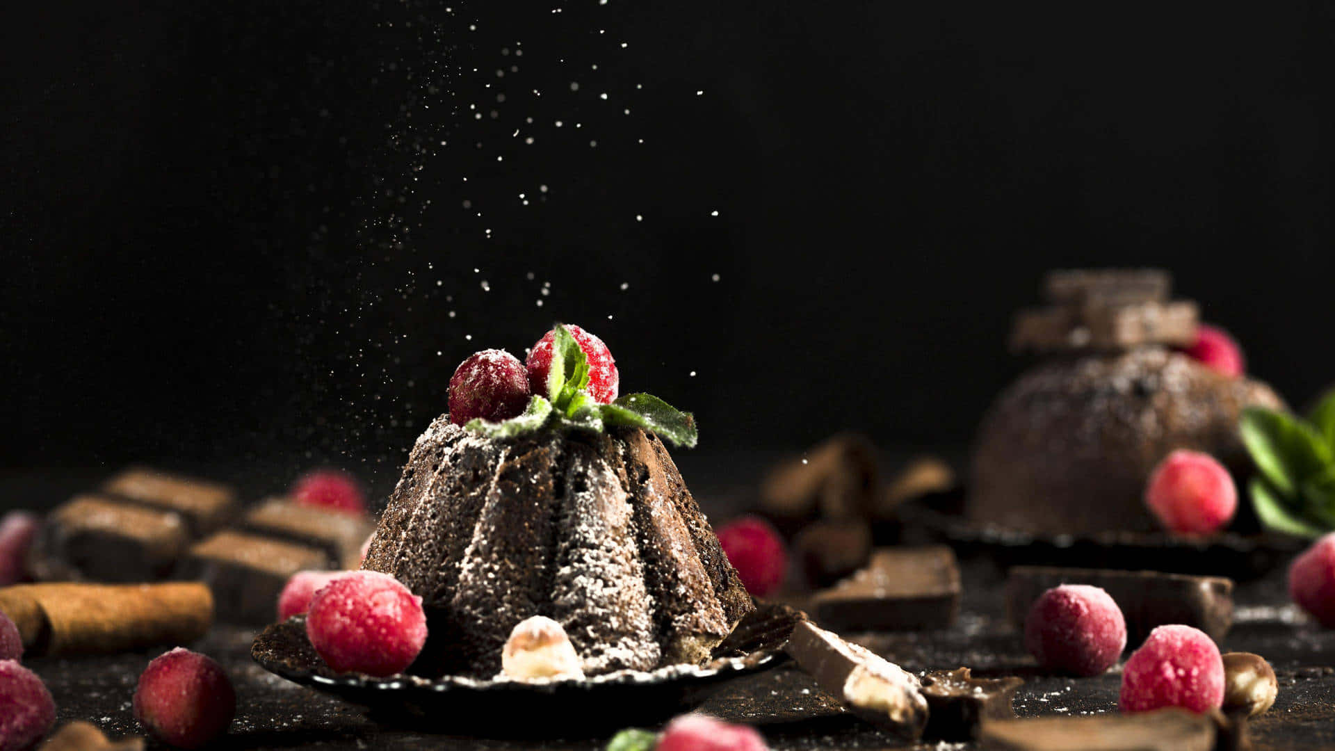 1920x1080 蛋糕背景：巧克力 Bundt 蛋糕 壁紙 — 一個豐富的朱古力熔岩蛋糕，撒上糖粉，並以新鮮覆盆子和薄荷裝飾，背景為深色。
