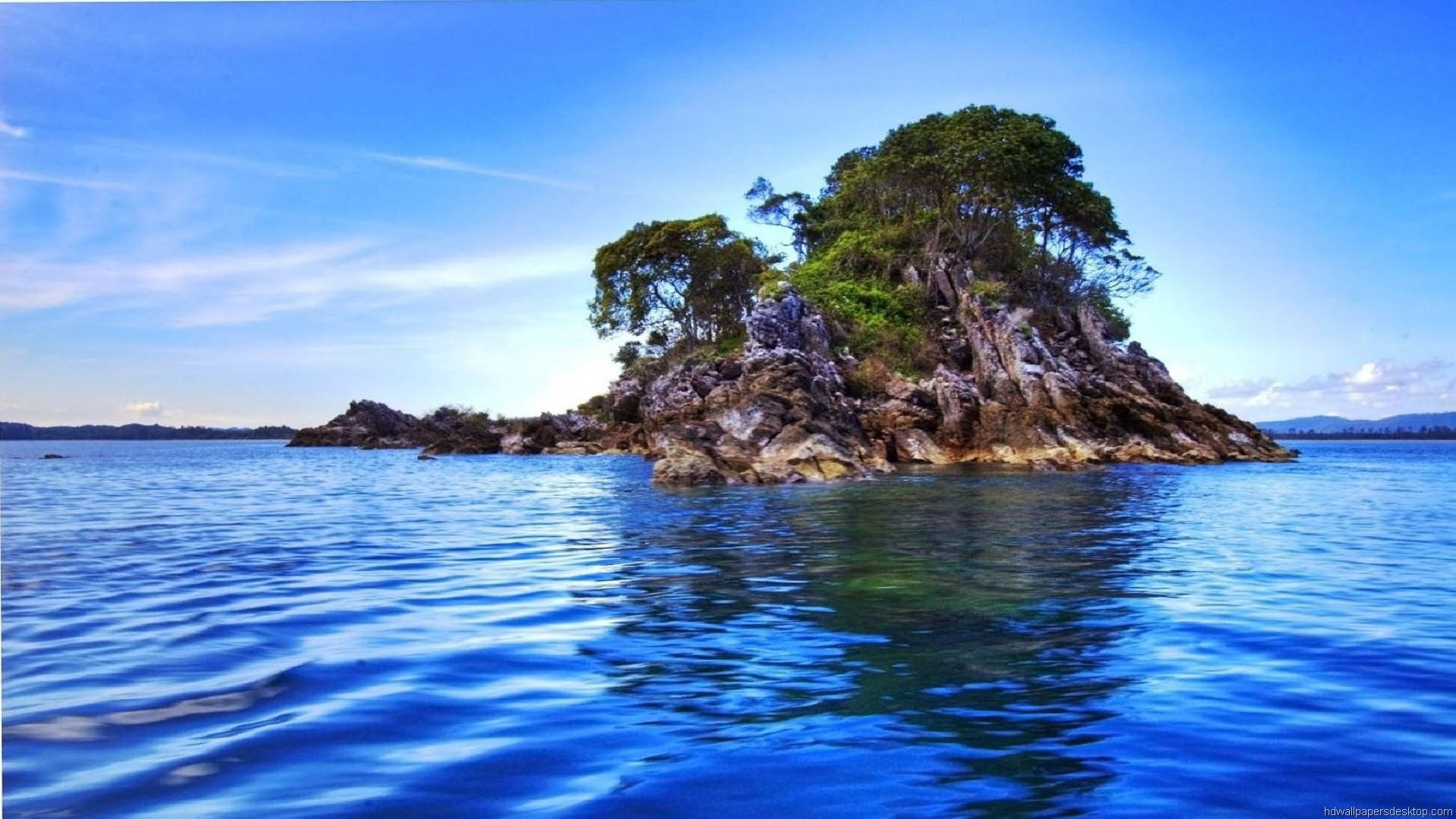 1920x1080 高清自然海島風景 壁紙 — 一個孤獨的岩石島嶼，長滿茂密的綠樹，從湛藍的海水中升起，天空晴朗。