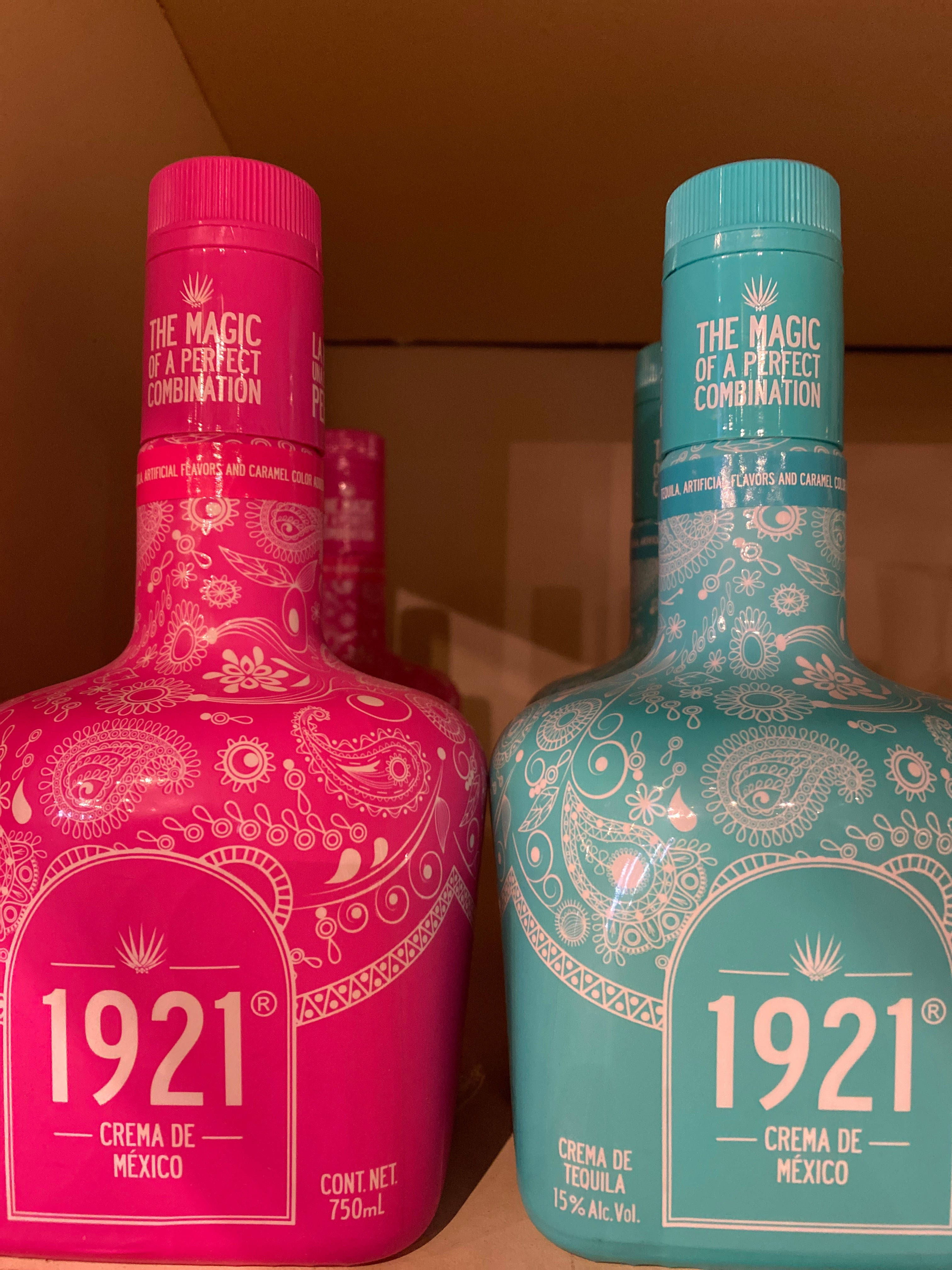 1921 蒂基拉 Amurala 與 Azul Maya 瓶身 壁紙 — 兩瓶色彩鮮豔的1921 Crema de Tequila，粉紅色和藍綠色，帶有複雜的白色圖案，並排放在一個紙板箱中。