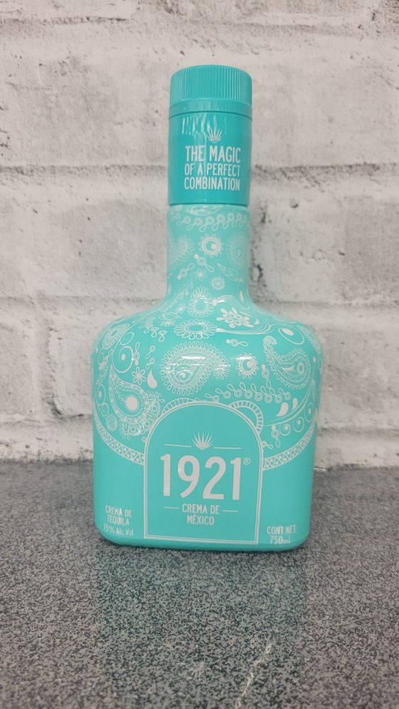 1921 蒂基拉 Azul Maya 瓶身貼於灰磚牆 壁紙 — 一個帶有白色佩斯利圖案的土耳其藍色1921 Crema de Mexico龍舌蘭酒瓶，放在灰色檯面上，背景是白色磚牆。