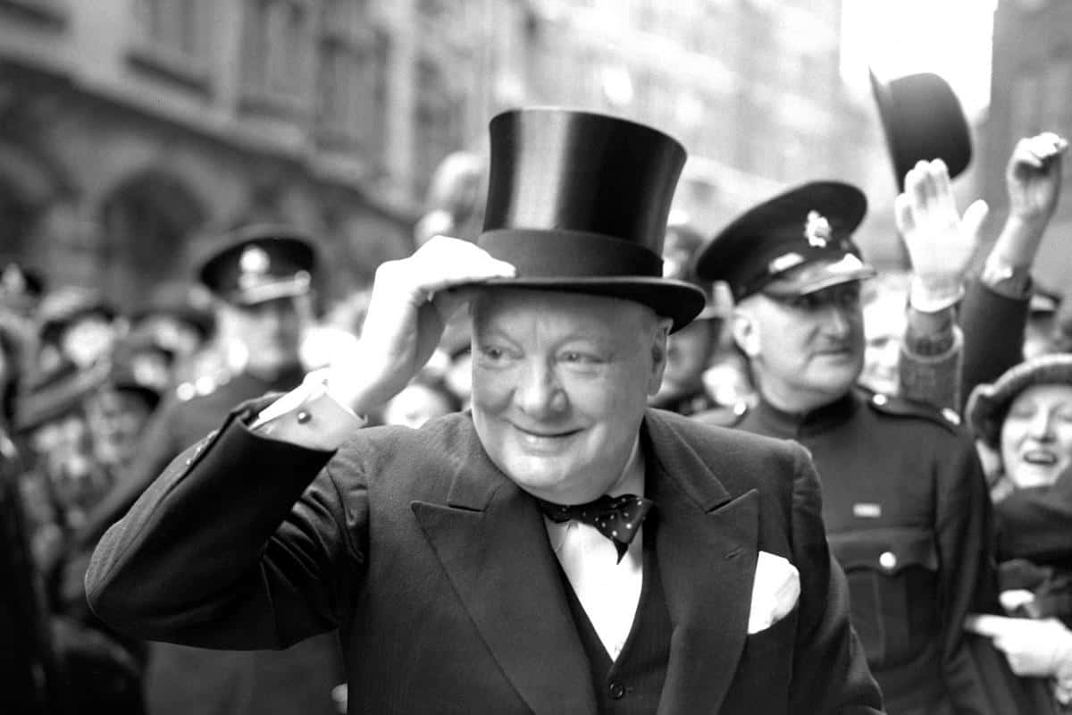 1940-1945 及 1951-1955 年擔任英國首相的溫斯頓·丘吉爾 壁紙 — 邱吉爾戴著高頂禮帽，在繁忙的城市街景中向人群致意。