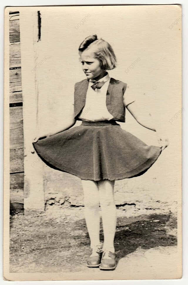 1940年代女孩旋轉裙擺 壁紙 — 一張復古棕褐色調的照片，一個穿著校服的年輕女孩在戶外木柵欄附近旋轉。