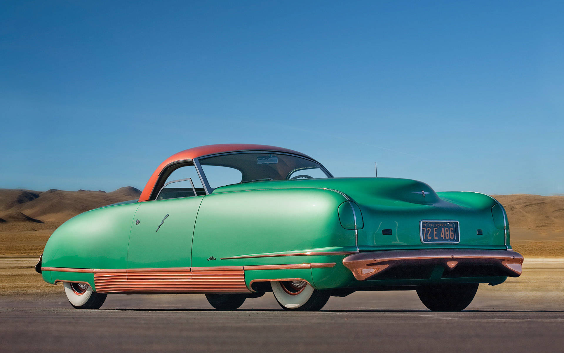 1941 Chrysler Thunderbolt – 古董汽車瑰寶 壁紙 — 一輛復古綠色和橙色車身、配備白色側壁輪胎的汽車，停在晴朗藍天下的沙漠公路上。