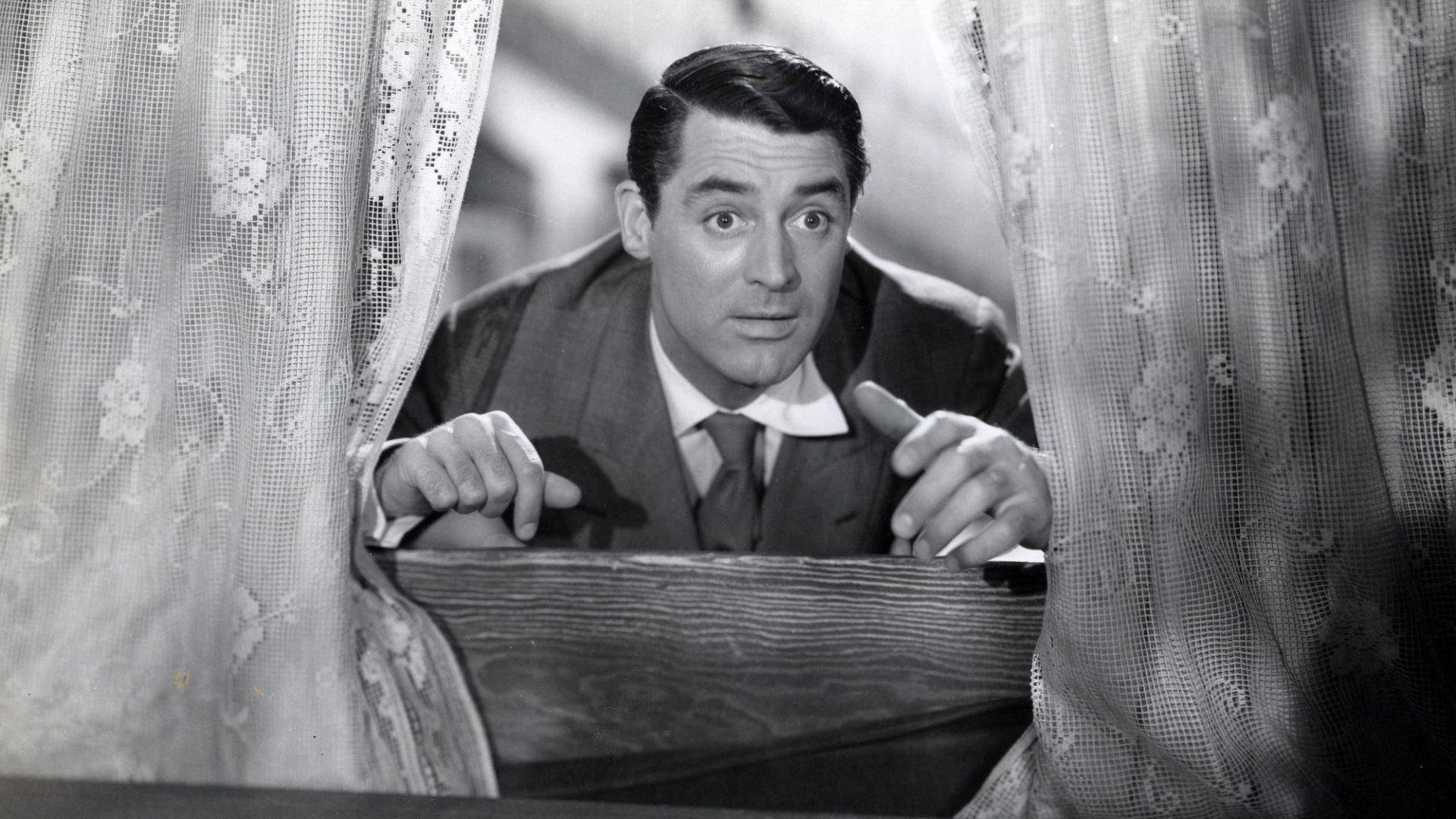 1944年電影《Arsenic and Old Lace》中的凱瑞·格蘭特 壁紙 — 一名身穿西裝的男子透過蕾絲窗簾窺視，睜大眼睛並用手指指點點，構成戲劇性的黑白場景。