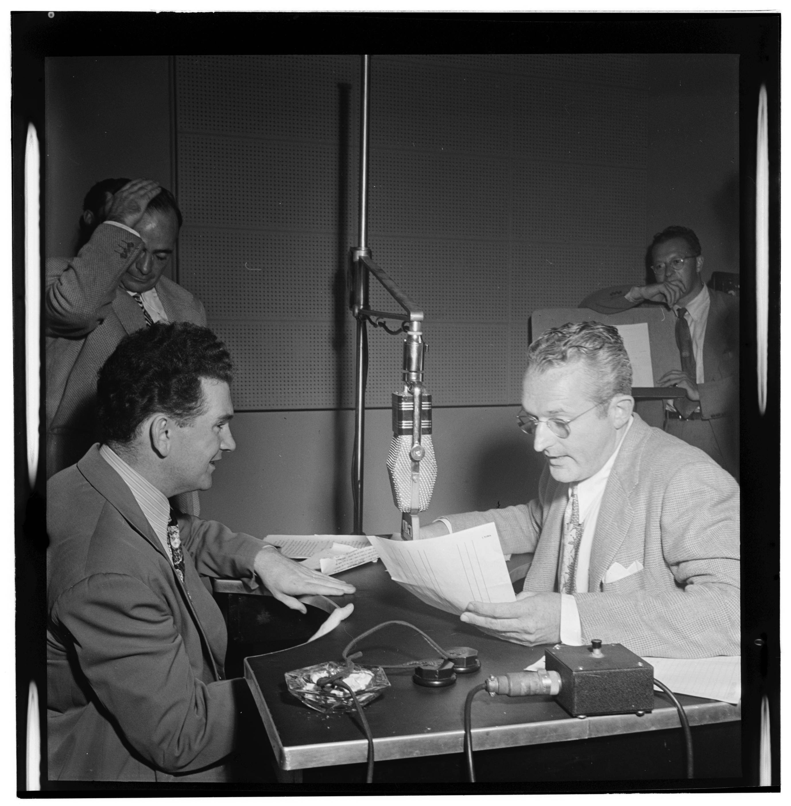 1947年湯米·多西電台演出黑白攝影 壁紙 — 兩名身穿西裝的男子在一個帶有大型麥克風和隔音牆的復古電台錄音室中交談。