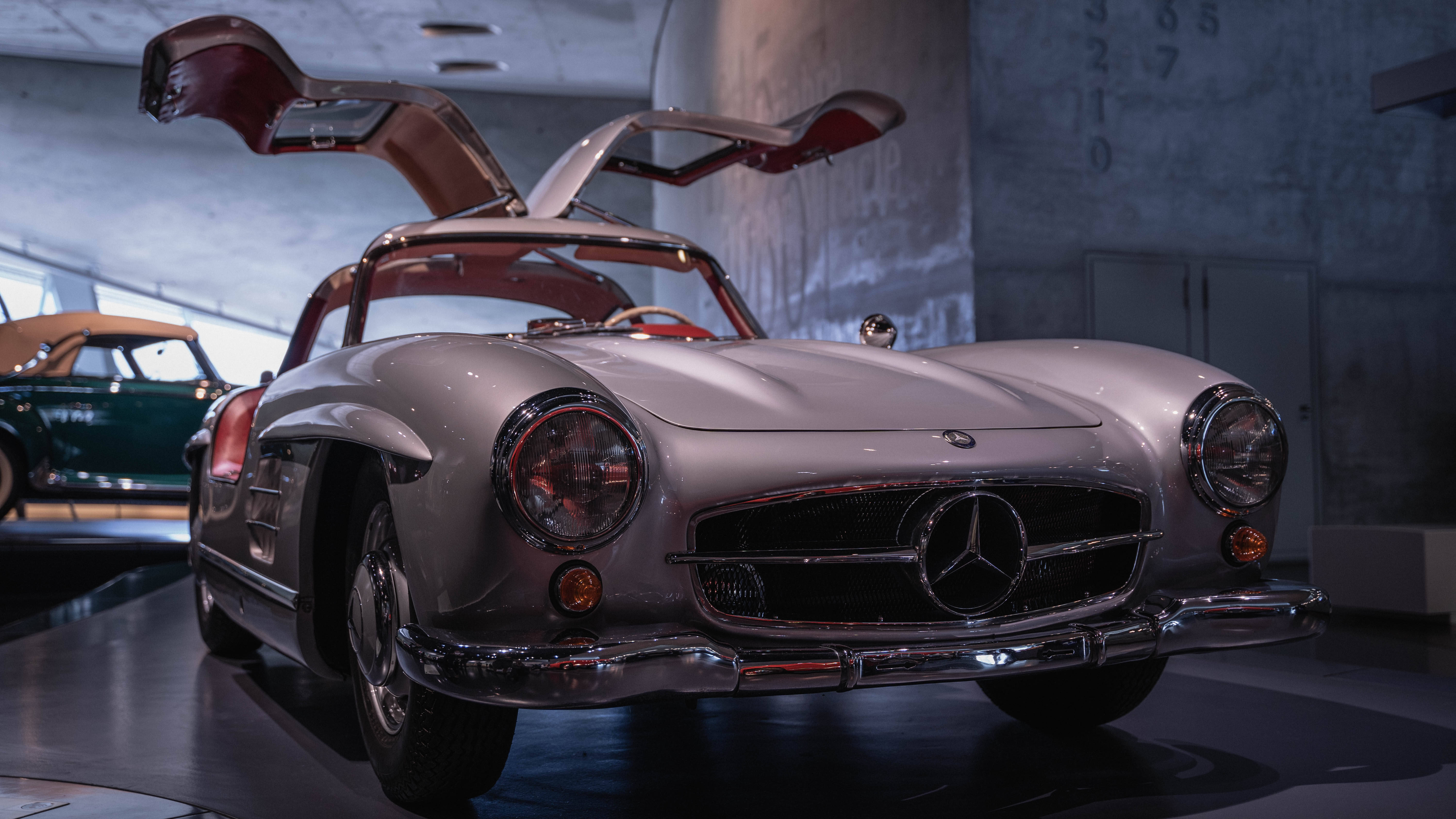 1954 梅賽德斯-奔馳 300 SL 展廳 壁紙 — 一輛銀色平治300 SL，鷗翼車門打開，在現代博物館中於戲劇性燈光下展出。