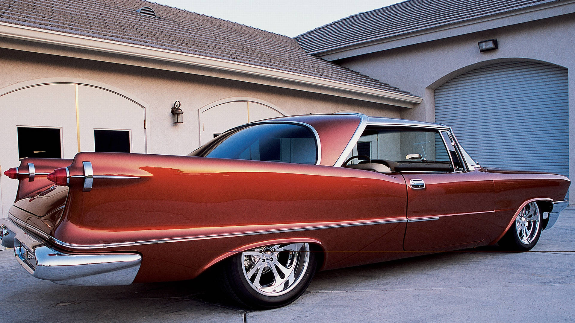 1957 Chrysler Imperial Custom 車款動態影像 壁紙 — 一輛光亮的銅色經典汽車，帶有鍍鉻尾翼和定制輪圈，停在帶有拱形車庫門的米色房屋前。