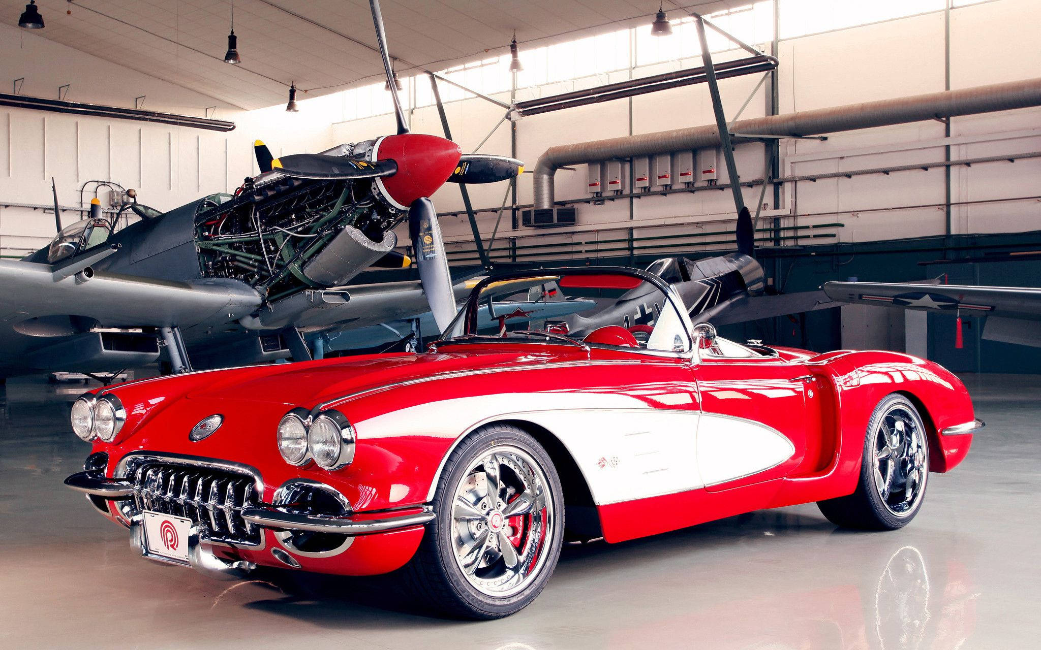 1959 年紅色雪佛蘭 Corvette 經典車 壁紙 — 一架光澤的紅白經典Corvette開篷車停泊在寬敞機庫內一架復古螺旋槳飛機旁邊。