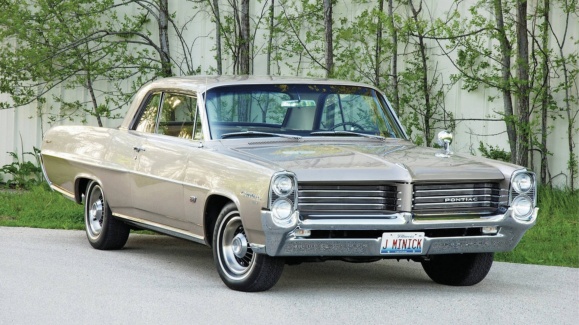 1963 Pontiac Catalina 車款 壁紙 — 一輛經典米色1960年代龐蒂亞克GTO雙門轎跑車在日光下閃閃發光，停在碎石路上，旁邊有綠樹。
