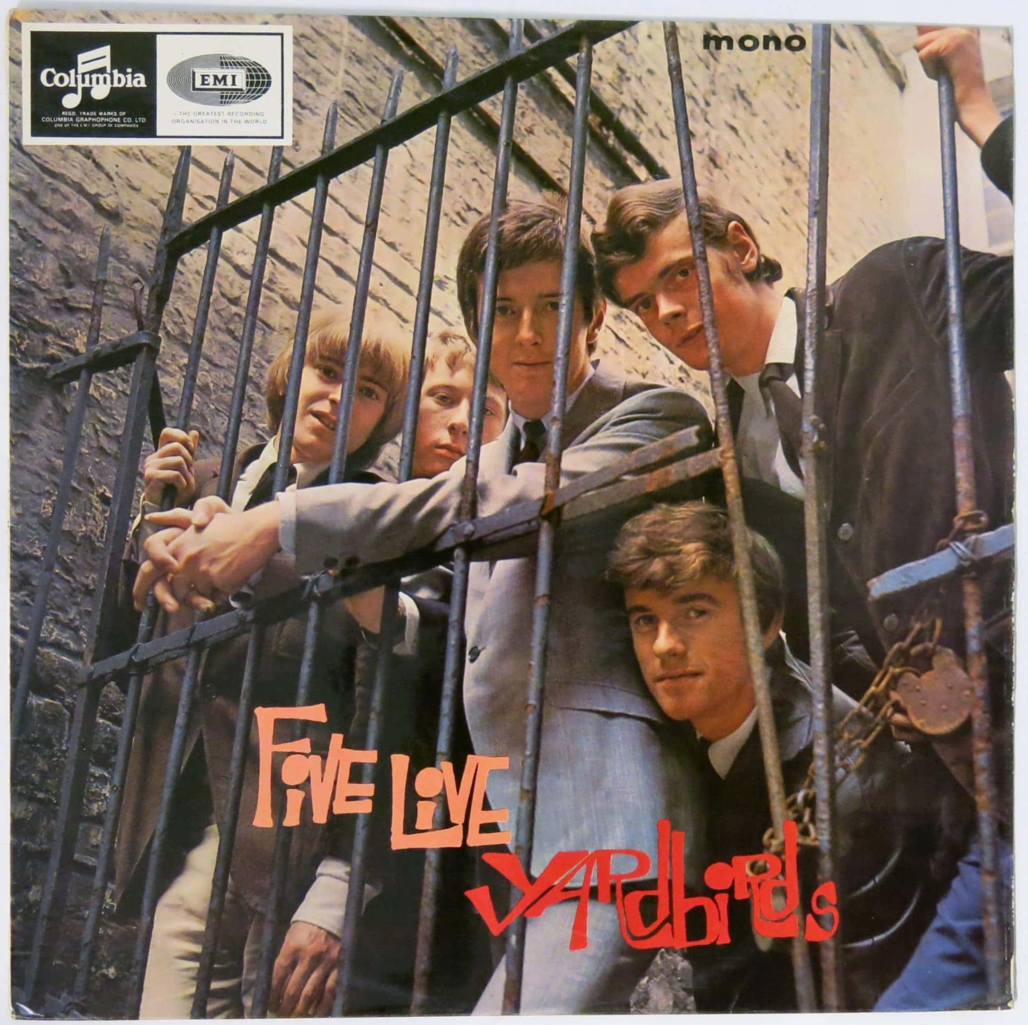 1964 年 Five Live Yardbirds 黑膠封面 壁紙 — 五位身穿西裝的年輕男子透過生鏽的金屬圍欄窺視，背景是磚牆，上面有醒目的橙色和紅色專輯文字。