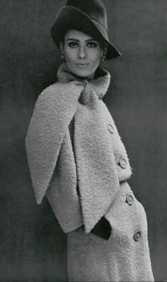1964年Jean Patou經典照片 壁紙 — 一位優雅的女士穿著質感外套和帽子，在復古工作室肖像中對著簡單背景擺姿勢。