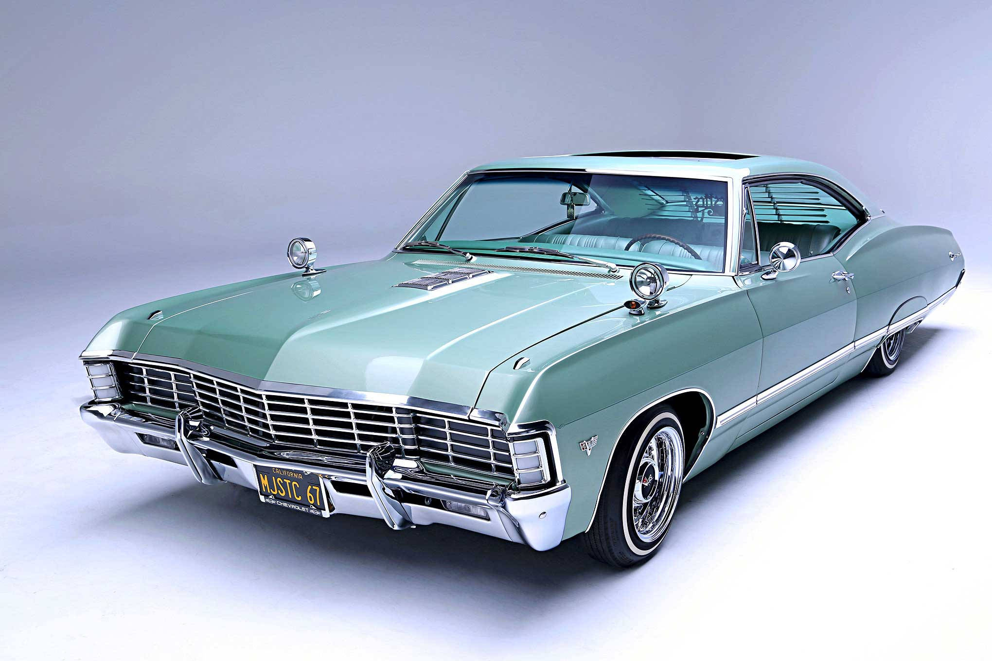 1967 年青綠色雪佛蘭 Impala - 經典優雅 壁紙 — 一輛薄荷綠色的經典美國肌肉車，帶有鍍鉻裝飾和白色輪胎，擺放在灰色工作室背景前。