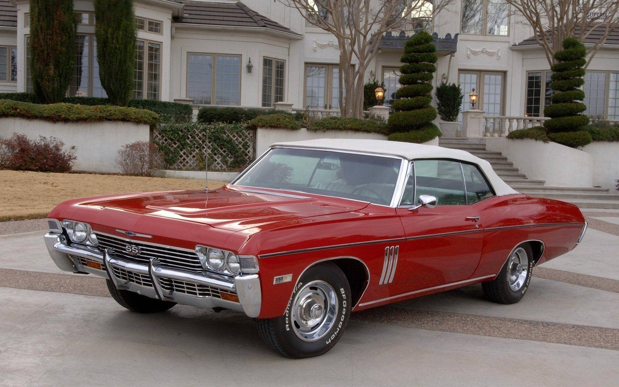 1967 年紅色雪佛蘭 Impala SS 壁紙 — 一架光澤紅色1967年雪佛蘭Chevelle SS開篷車，白色車頂，停泊在豪華大宅前的瓷磚車道上。