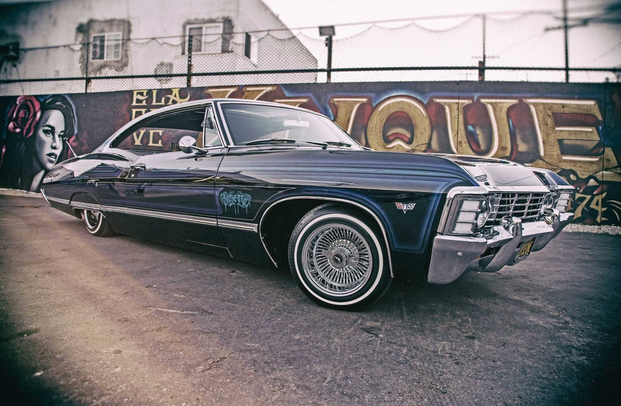 復古優雅：1967年雪佛蘭Impala 壁紙 — 一輛時尚的黑色經典肌肉車，帶有鍍鉻細節，停在充滿活力的塗鴉牆前。