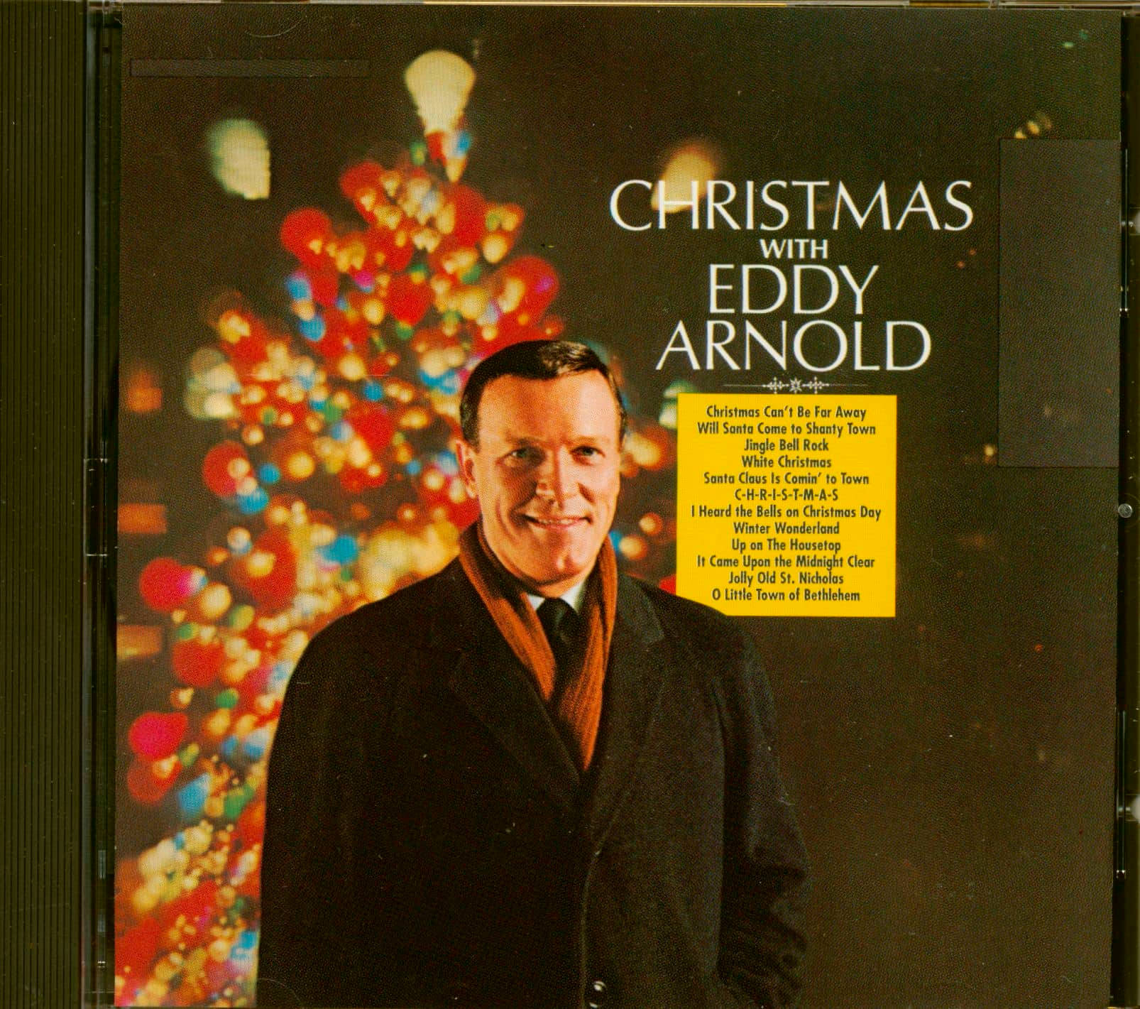 Eddy Arnold 穿著深色外套和橙色圍巾，在節日聖誕樹前微笑。