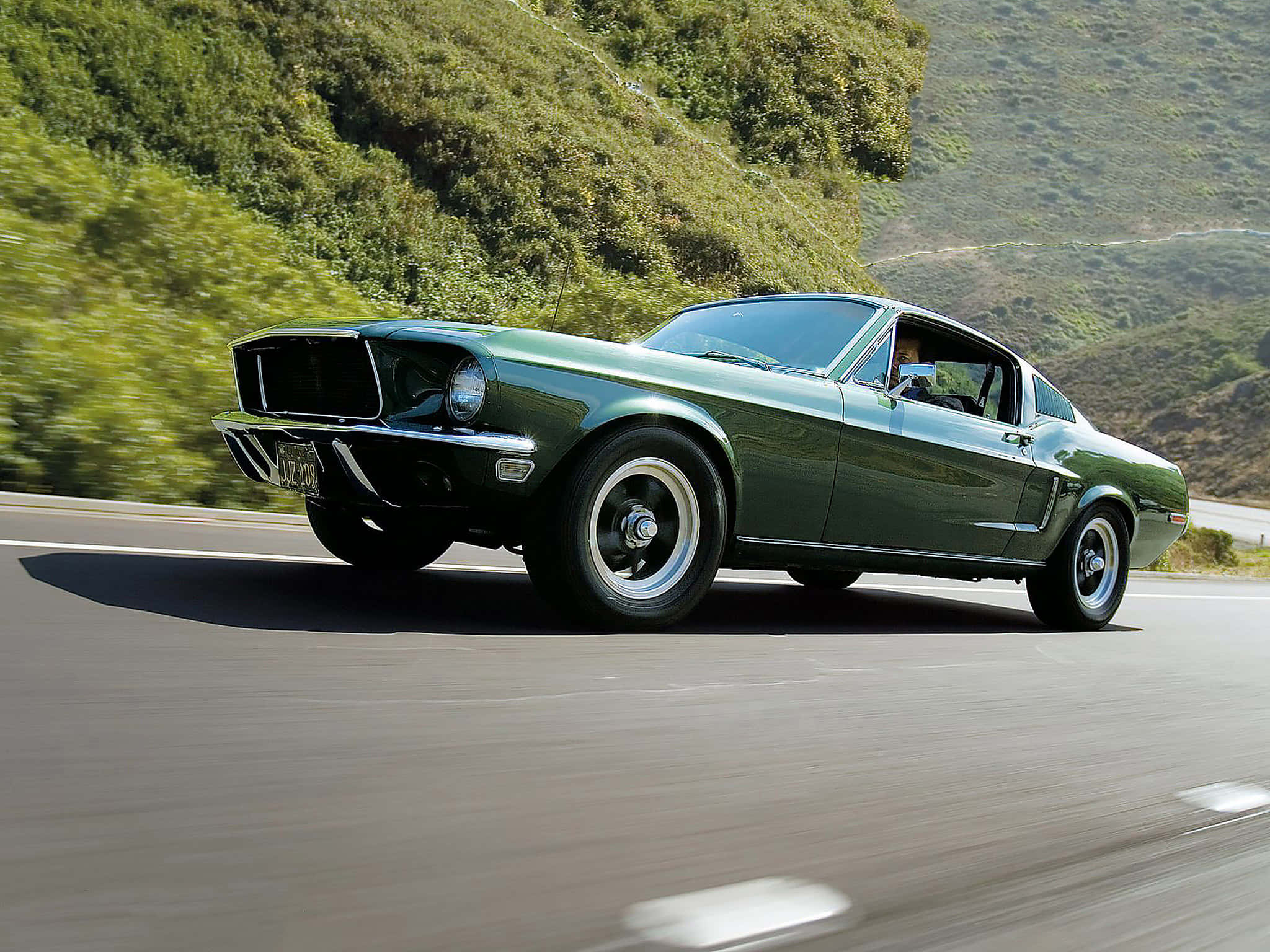 1968款福特野馬GT快背肌肉車 壁紙 — 一架經典綠色野馬跑車沿著蜿蜒的山路行駛，兩旁翠綠的山坡飛掠而過。