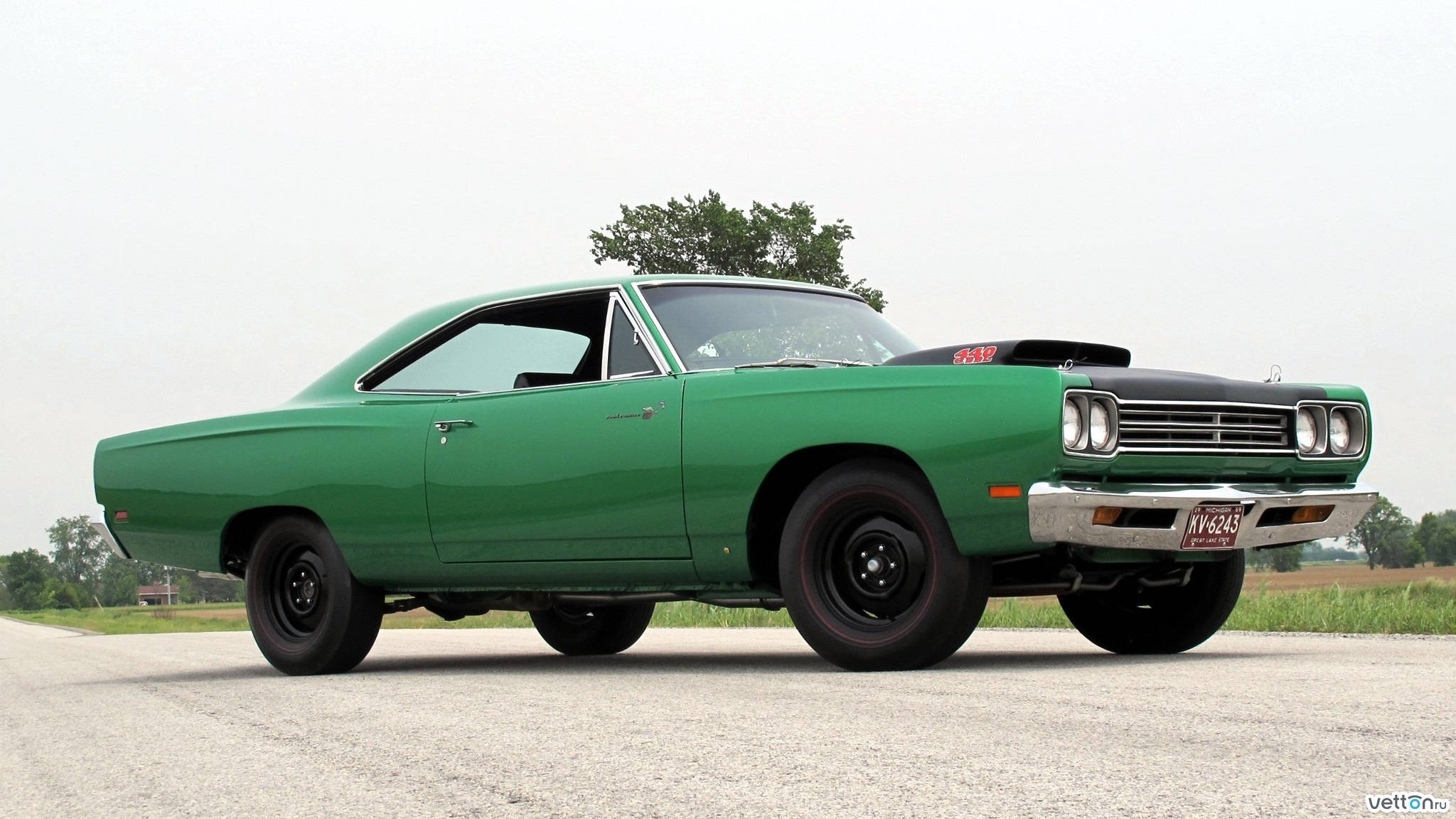 1969年普利茅斯Road Runner 硬頂綠色車款 壁紙 — 一輛充滿活力的綠色經典肌肉車，帶有黑色引擎蓋和車輪，停在碎石路上，天空多雲。