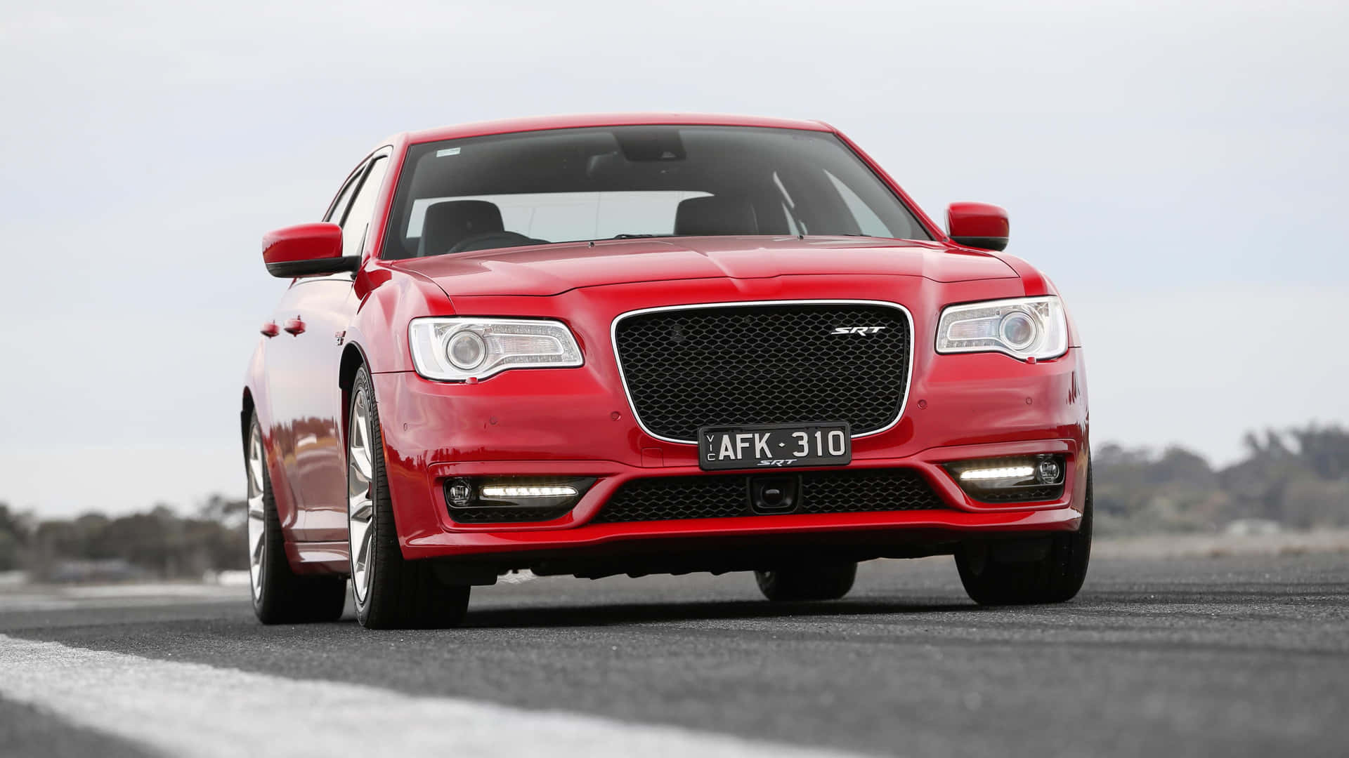 多雲天空下開闊道路上的紅色Chrysler 300 SRT房車。